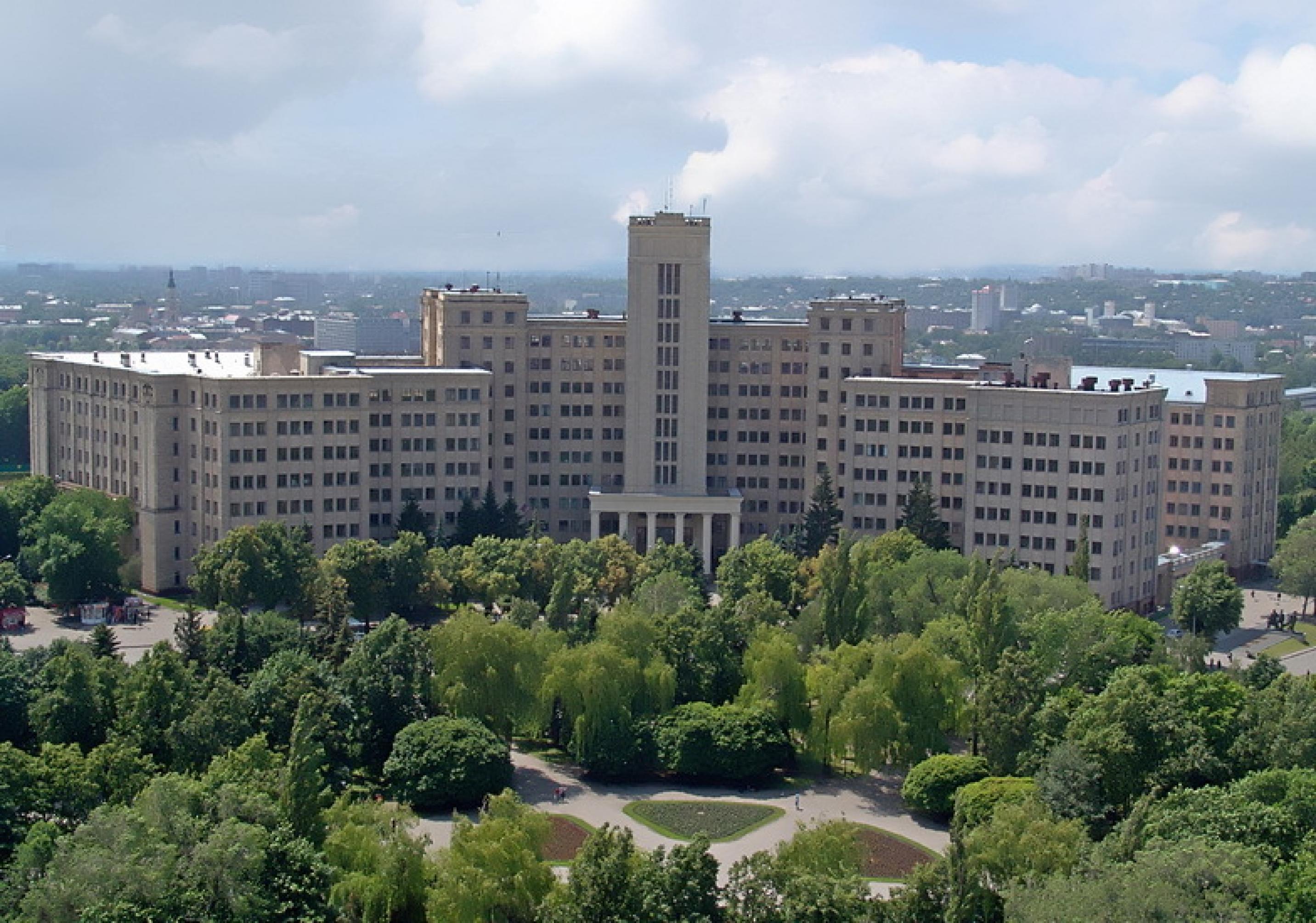 Ein großes, mehrstöckiges, grauen Universitätsgebäude umgeben von grünen Bäumen.
