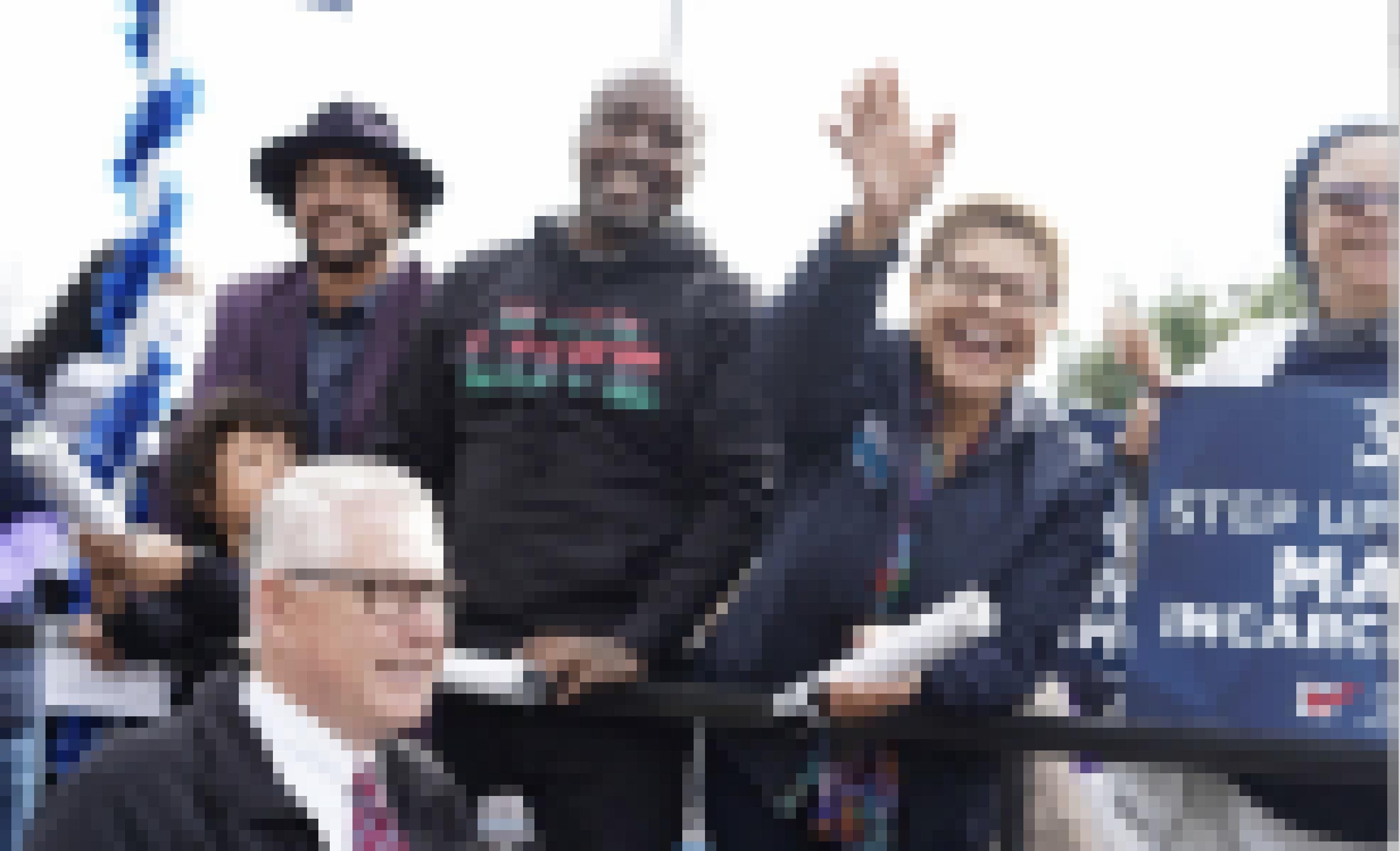 Karen Bass, steht zwischen Aktivisten, einer im Sweatshirt, der andere mit Anzug und Hut, wieder eine andere mit Kopftuch und Brille auf einem Bus. Sie winkt lachend Anhängern zu..