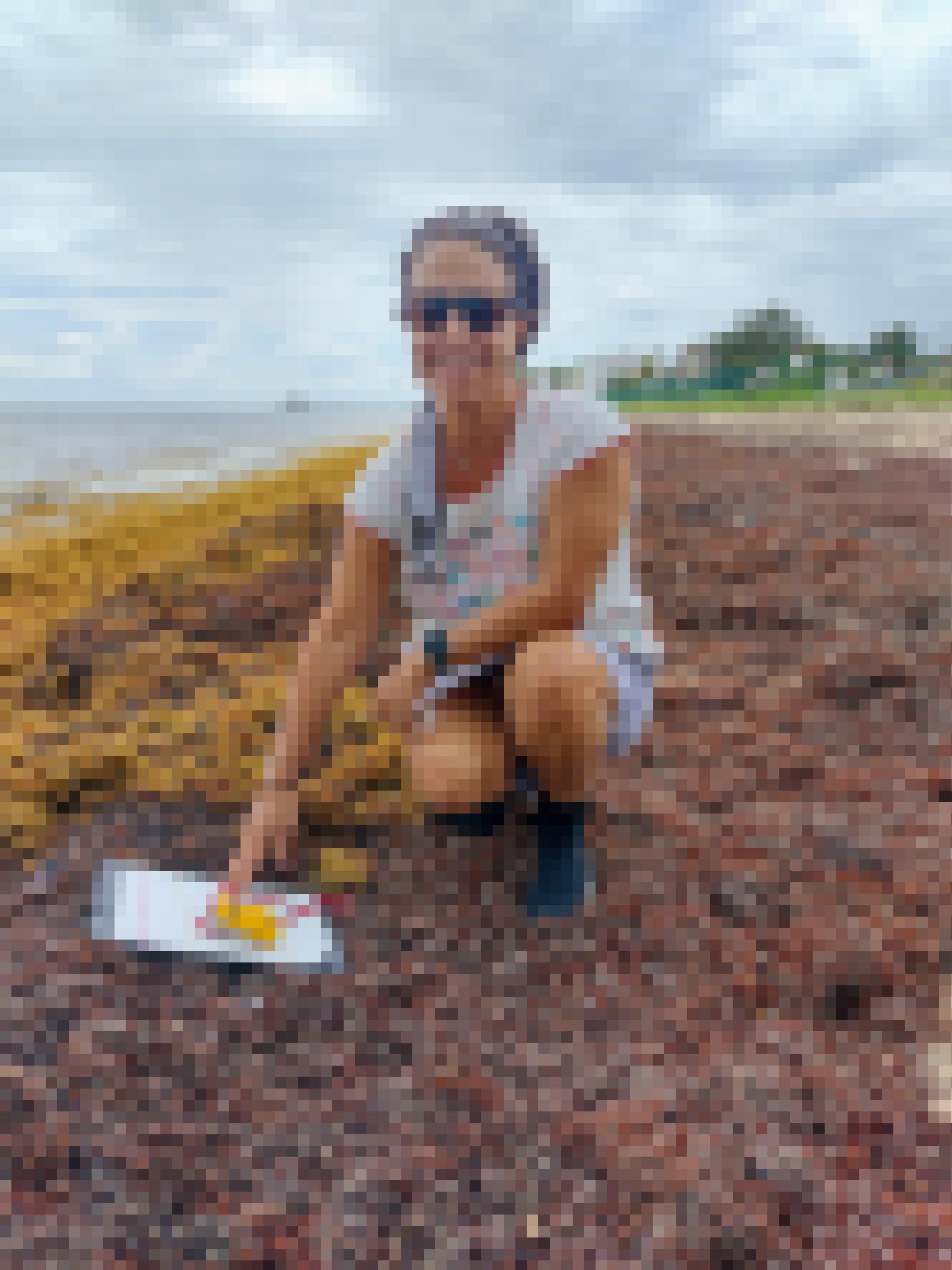 Forscherin Rosa Rodriguez mit Block und Messgerät inmitten von Algenbergen am Strand.
