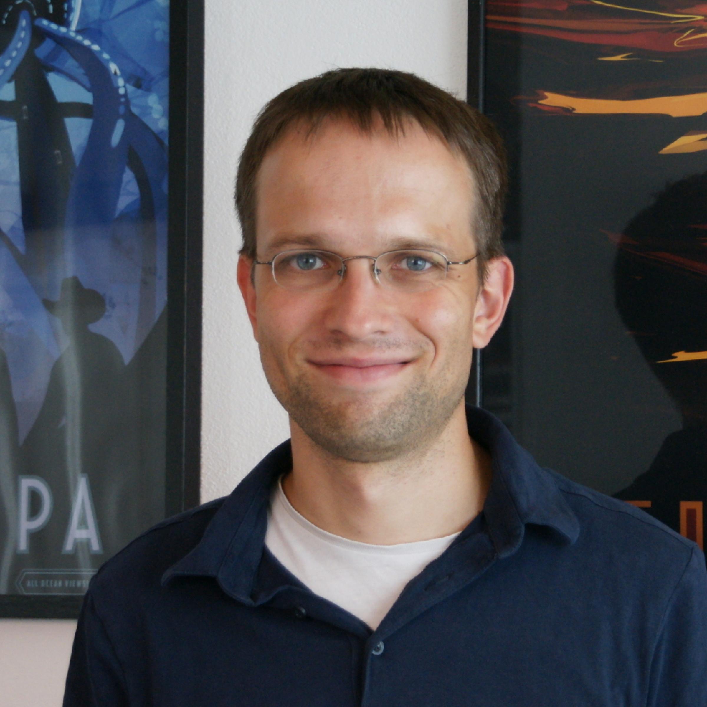 Karl Urban steht vor einer Wand mit zwei Plakaten: Mond Europa und Titan