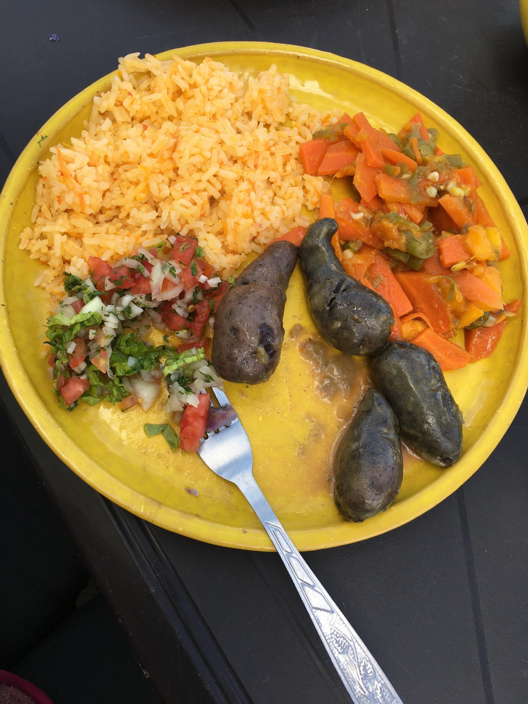 Ein Teller mit gelbem Reis, Salat aus kleingeschnittenem Koriander, Tomate, Zwiebel, Gemüse aus grünen Bohnen und Karotten und kegelartigen Kartoffeln.