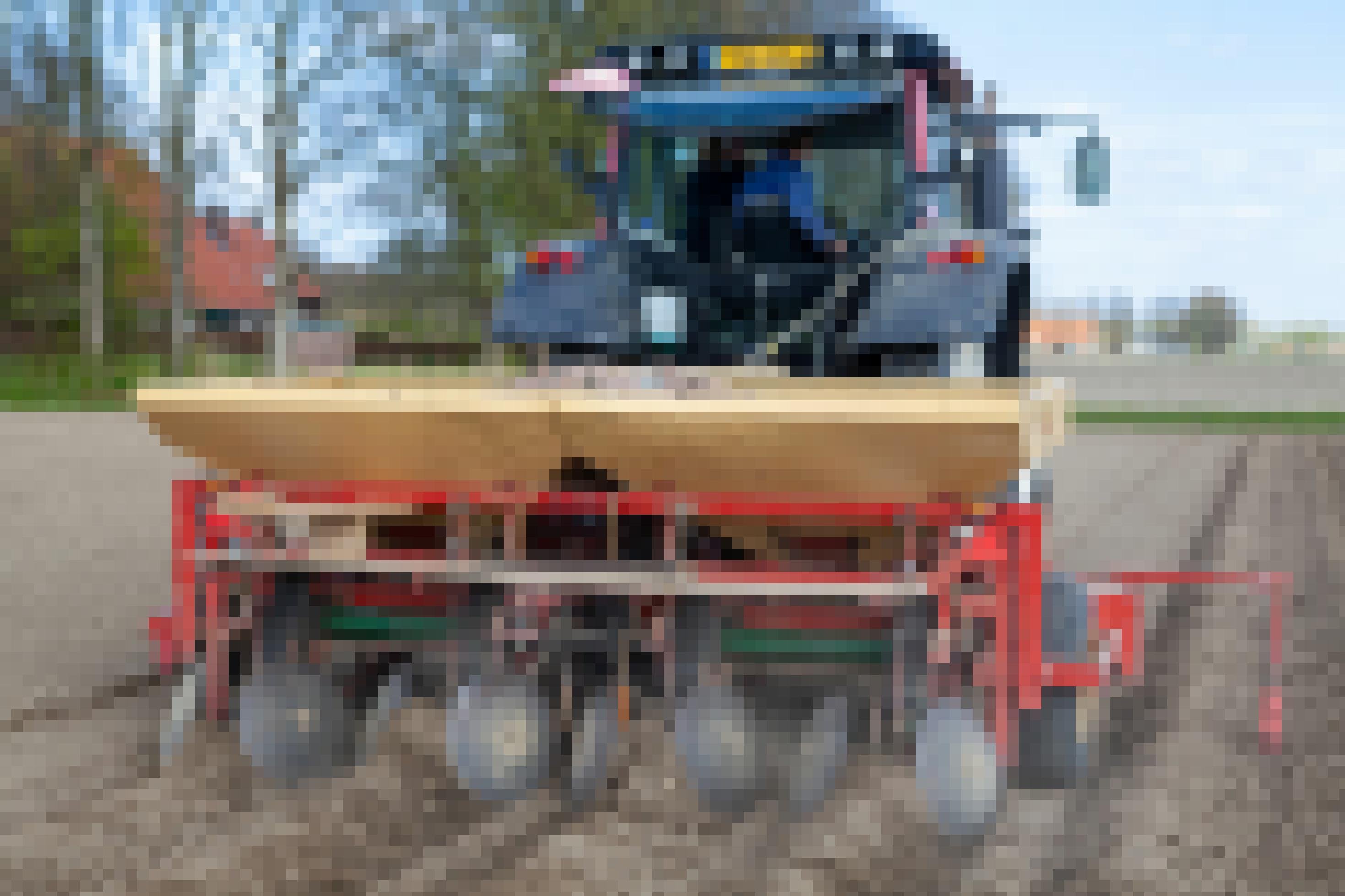 Eine Kartoffelpflanzmaschine von hinten, als Anhänger an einem Traktor. Fährt auf einem ebenen, braunen Feld voller Furchen.