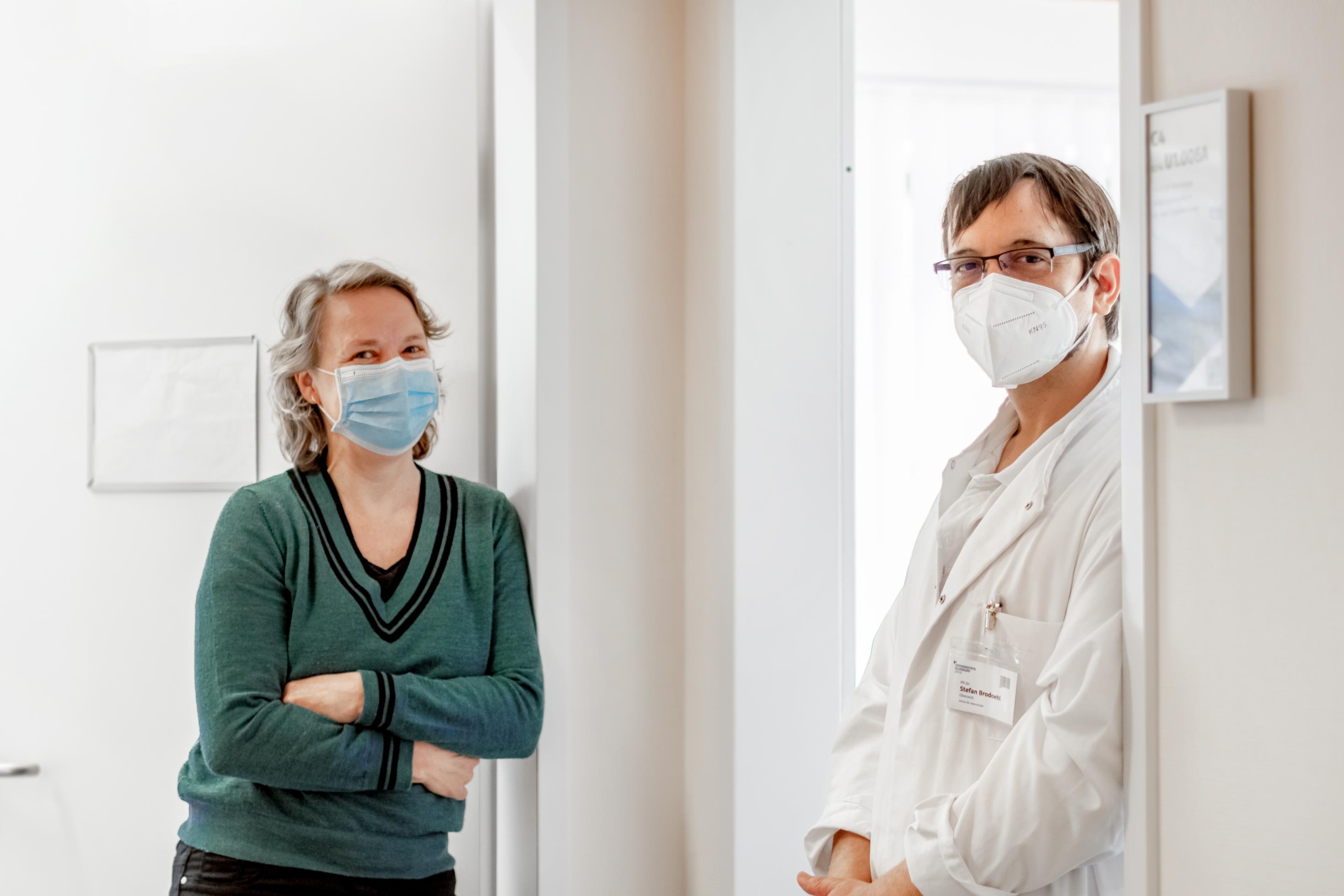 Eine Frau und ein Mann stehen an einer Tür angelehnt, beide tragen einen Mund-Nasenschutz. Die Therapeuten kümmern sich um Long Covid Patienten.