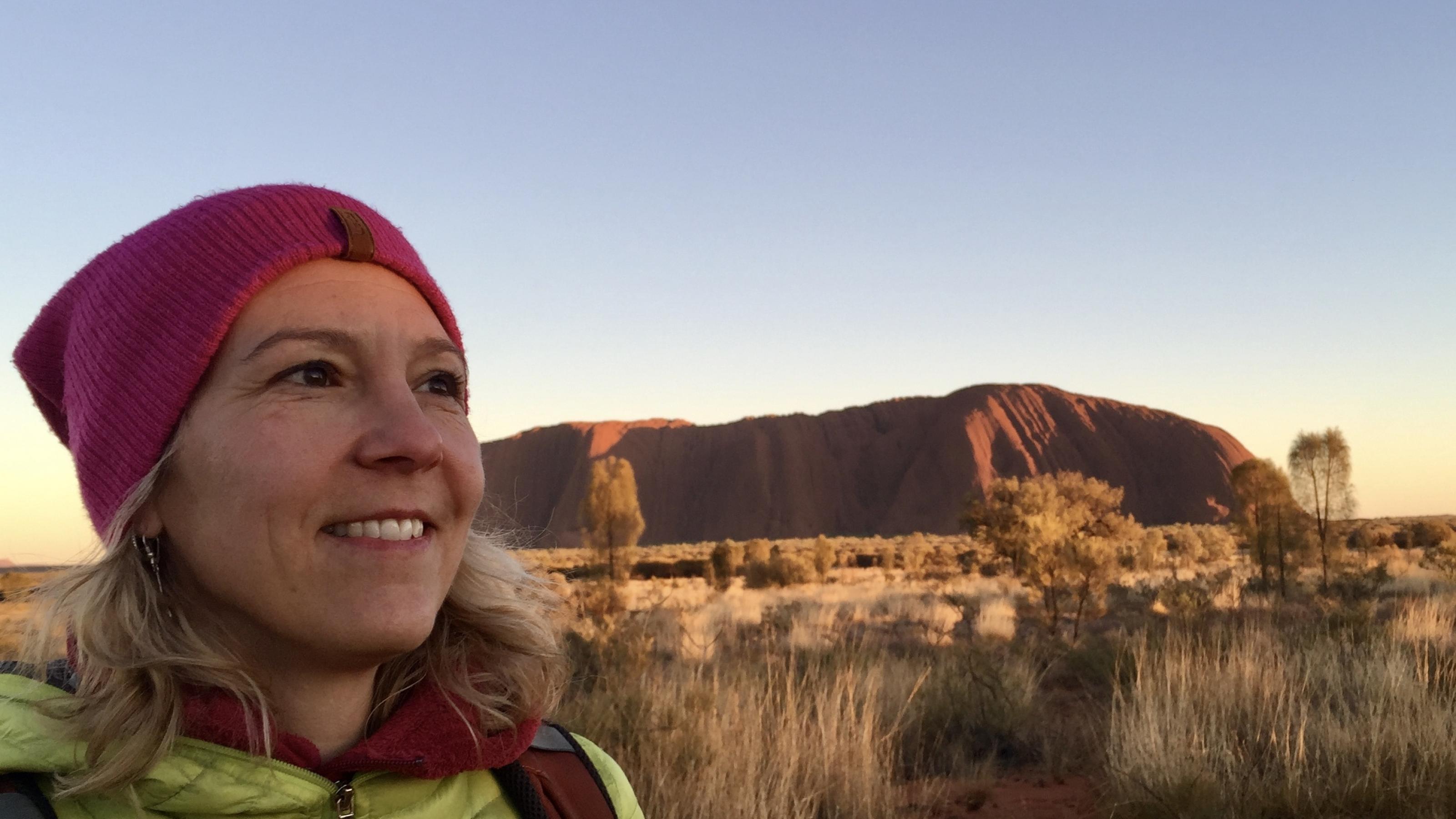 Das Bild zeigt Katja Trippel bei Sonnenaufgang vor dem Uluru