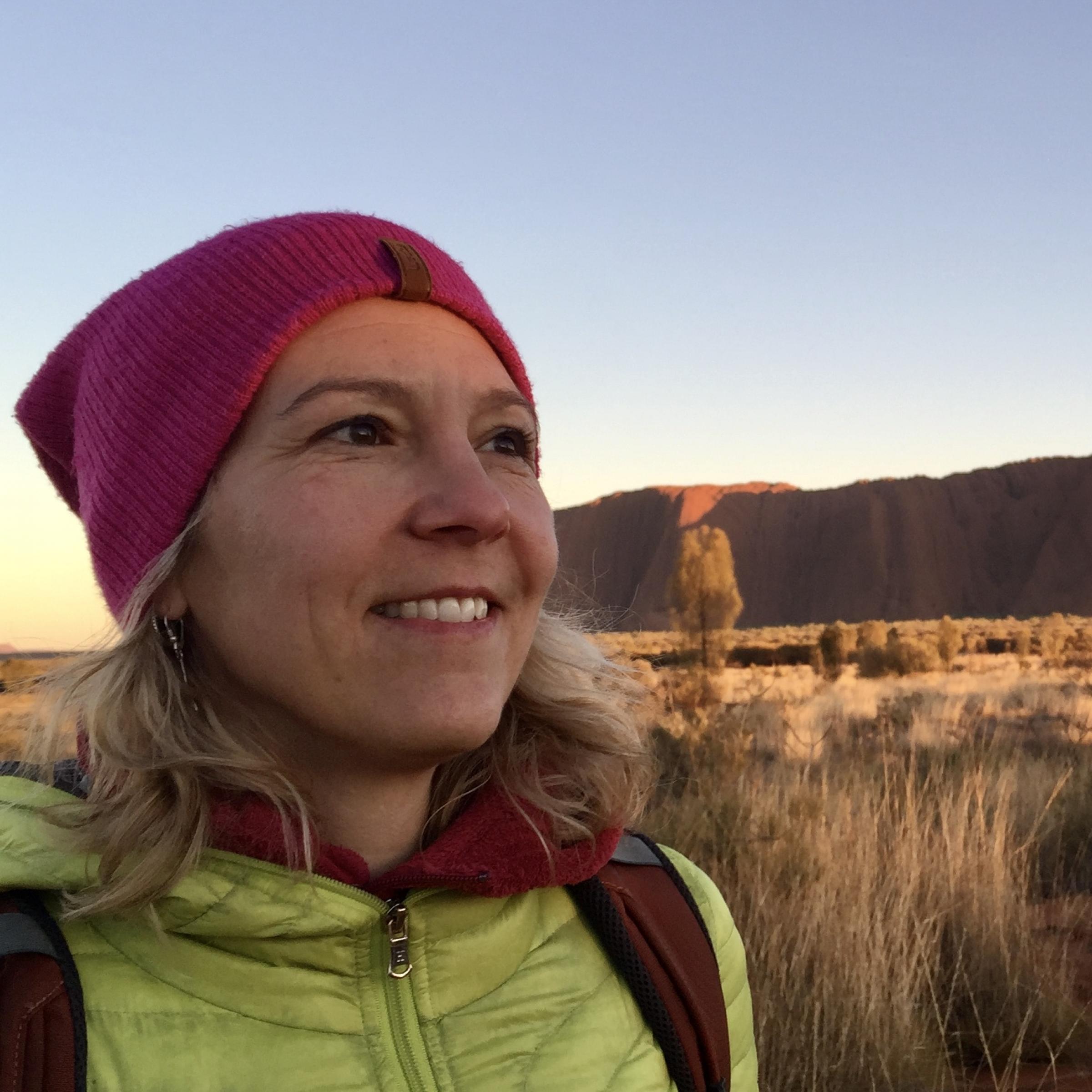 Das Bild zeigt Katja Trippel bei Sonnenaufgang vor dem Uluru.