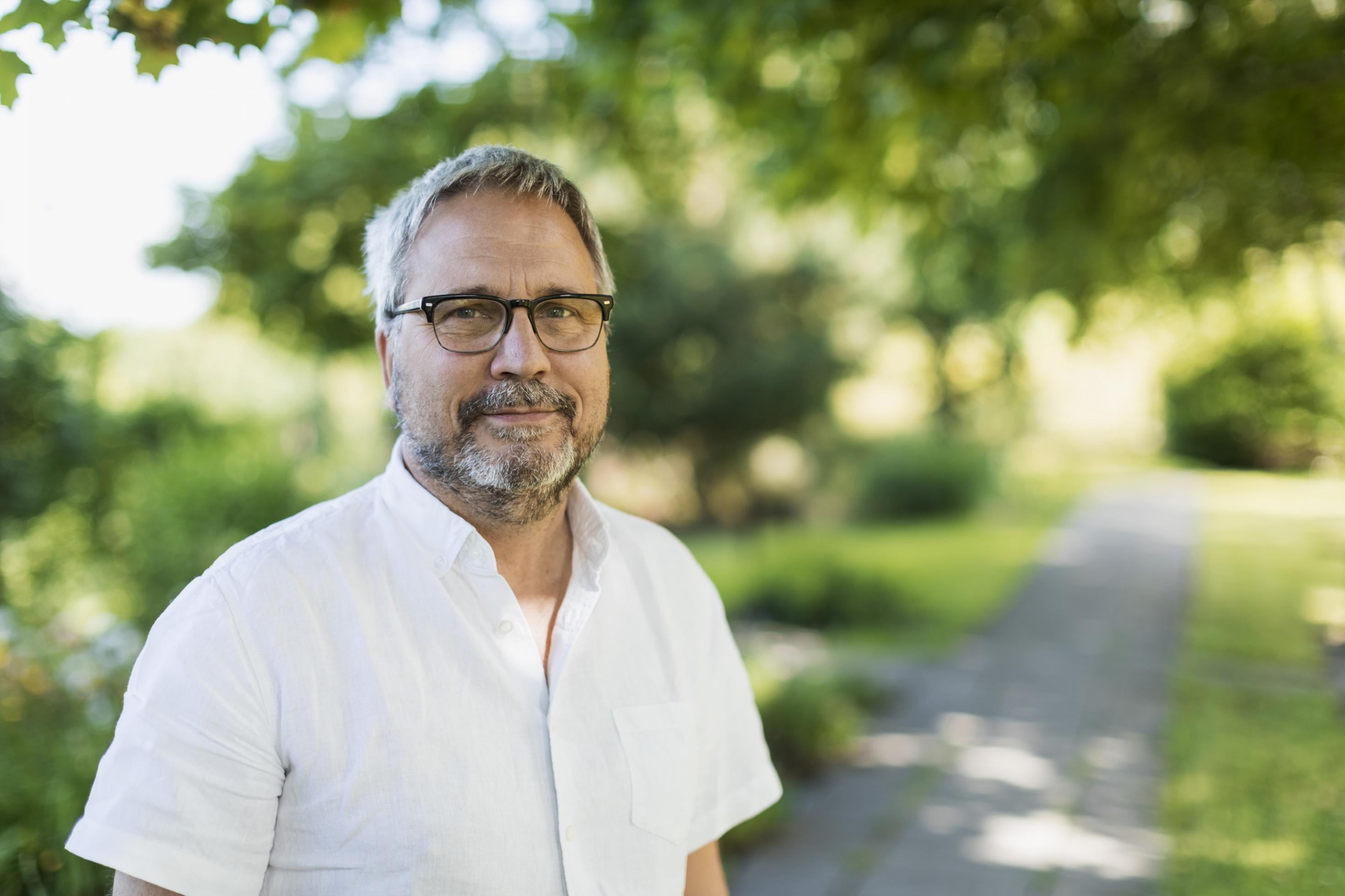 Porträtfoto eines Mannes mit grauem Haar und Vollbart, weißes Hemd