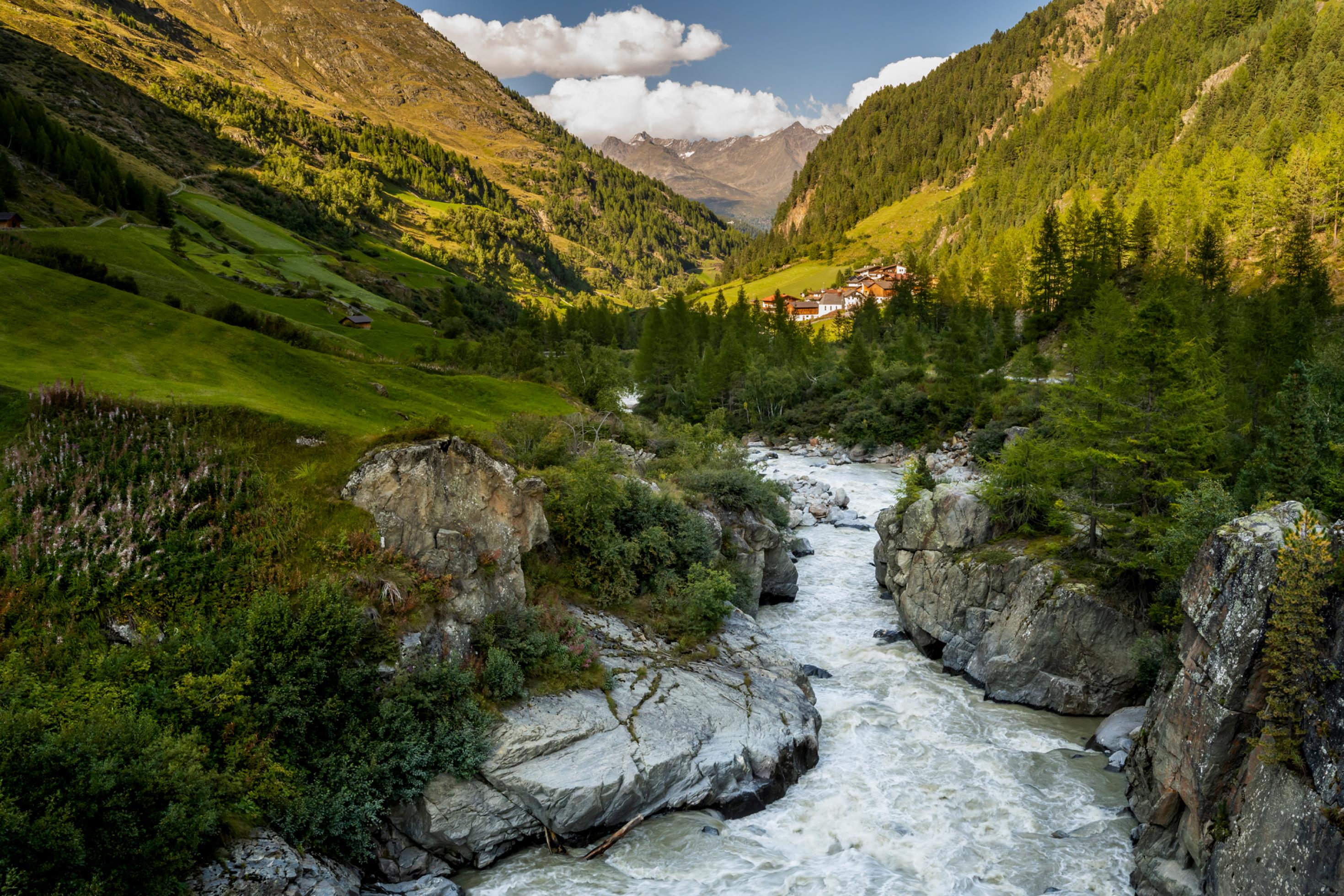 Gebirgsbach zwischen Felsen in einem engen, grünen Alpental