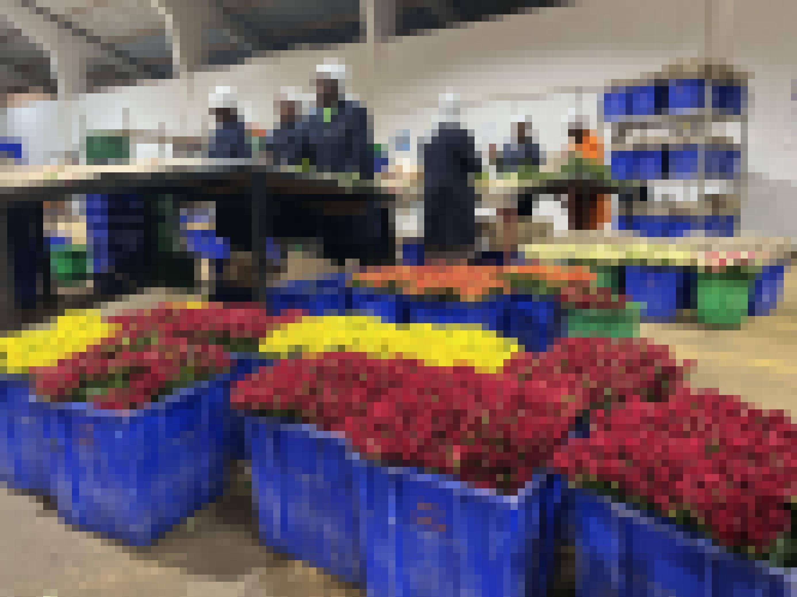 Arbeiterinnen in blauer Arbeitskleidung im Hintergrund, im Vordergrund blaue Eimer mit einem Meer von Rosen.