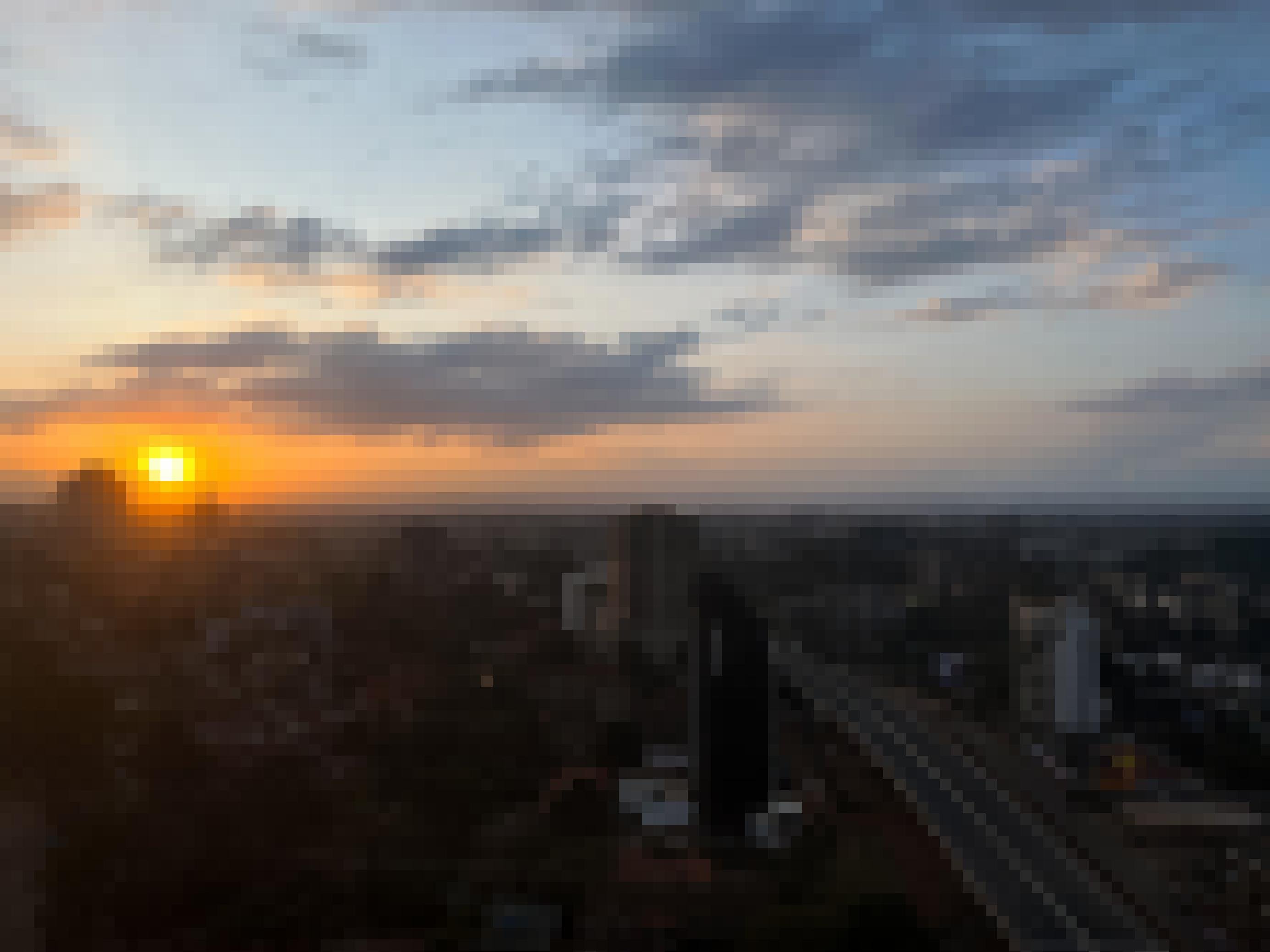 Ein Blick über die Stadt, die Sonne geht gerade unter. Etliche Hochhäuser säumen den neuen Expressway, der tief unter der Position des Betrachtenden liegt.