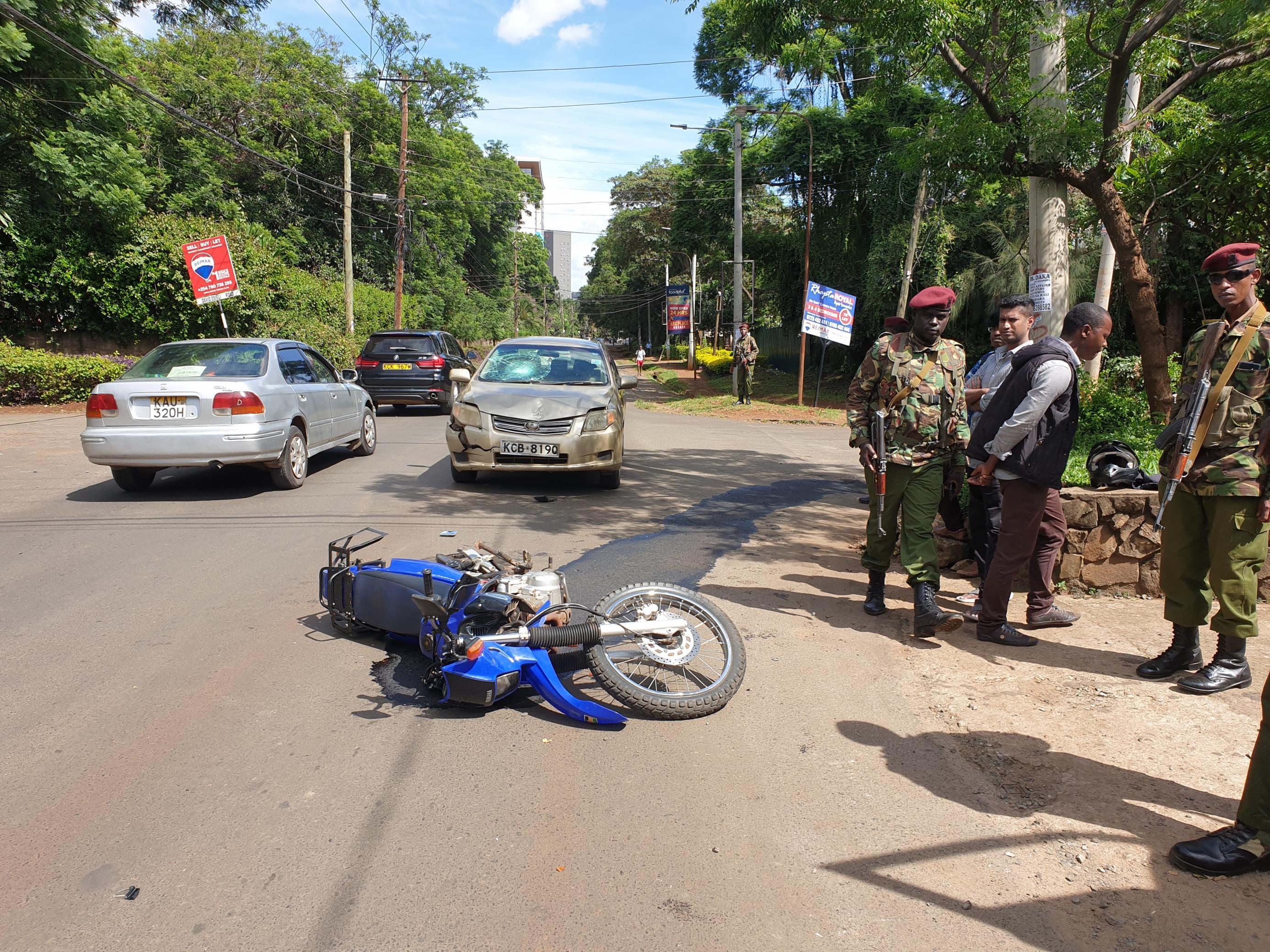 Zu sehen sind ein leicht beschädigter PKW, ein Motorrad, das davor auf der Straße liegt und am Rand einige Polizisten.