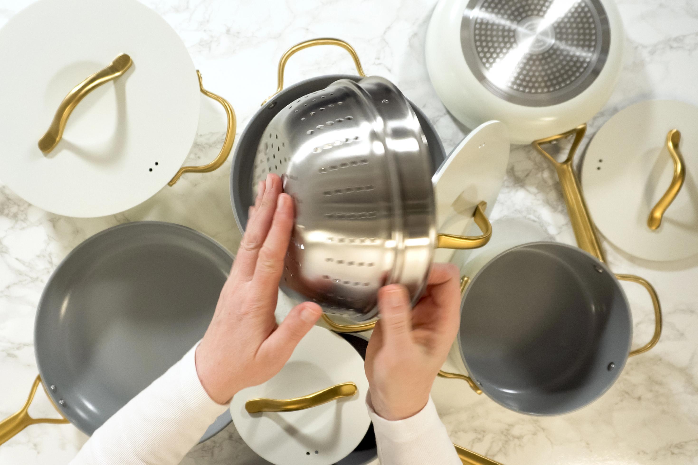 Draufsicht: Weißes Kochgeschirr, unklar ist, ob es sich um echtes Keramik handelt. Frauenhand hat ein Sieb aus Edelstahl in der Hand.