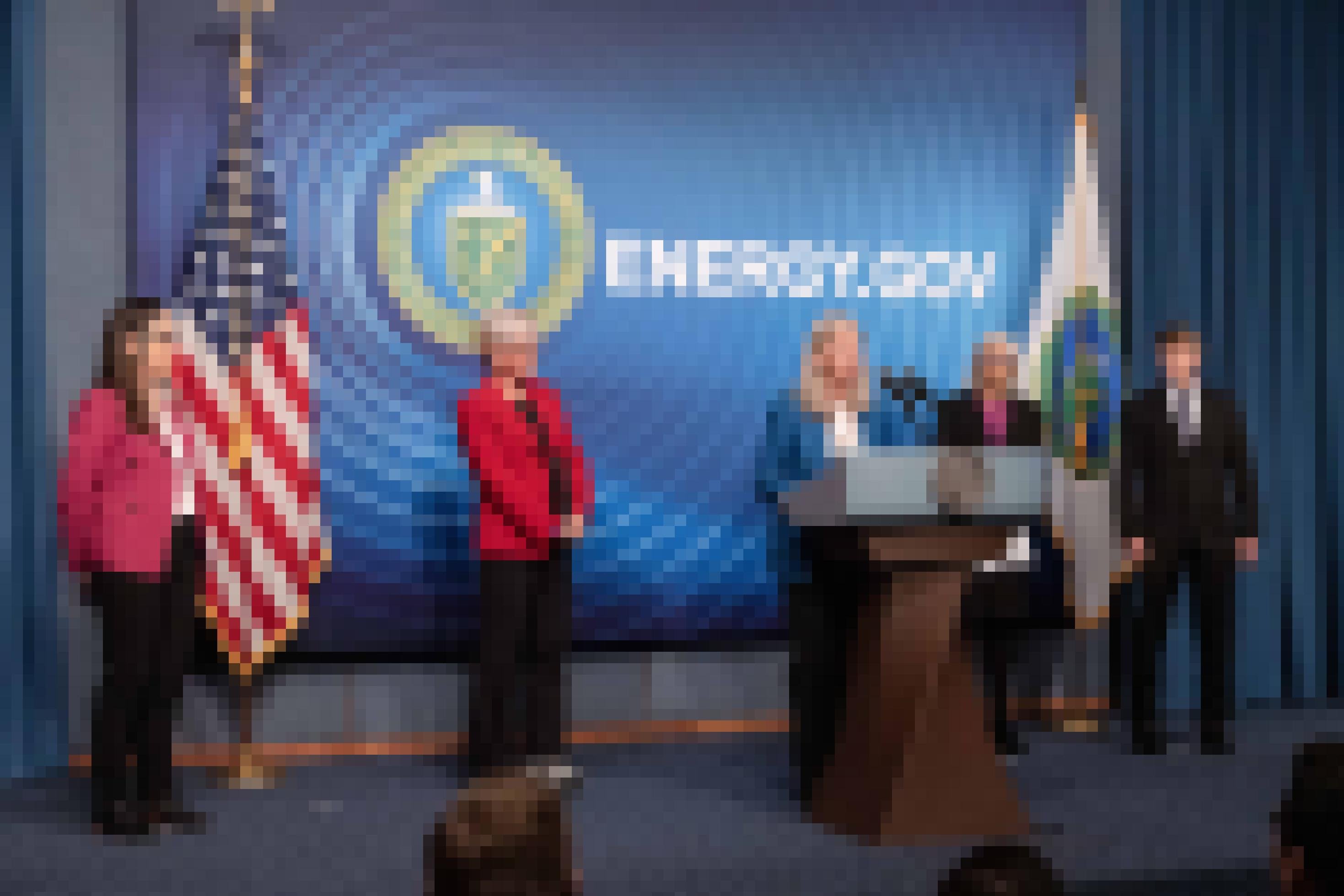 Frauen in Businesskleidung mit US-Fahne, eine am Rednerpult dahinter steht energy.gov.