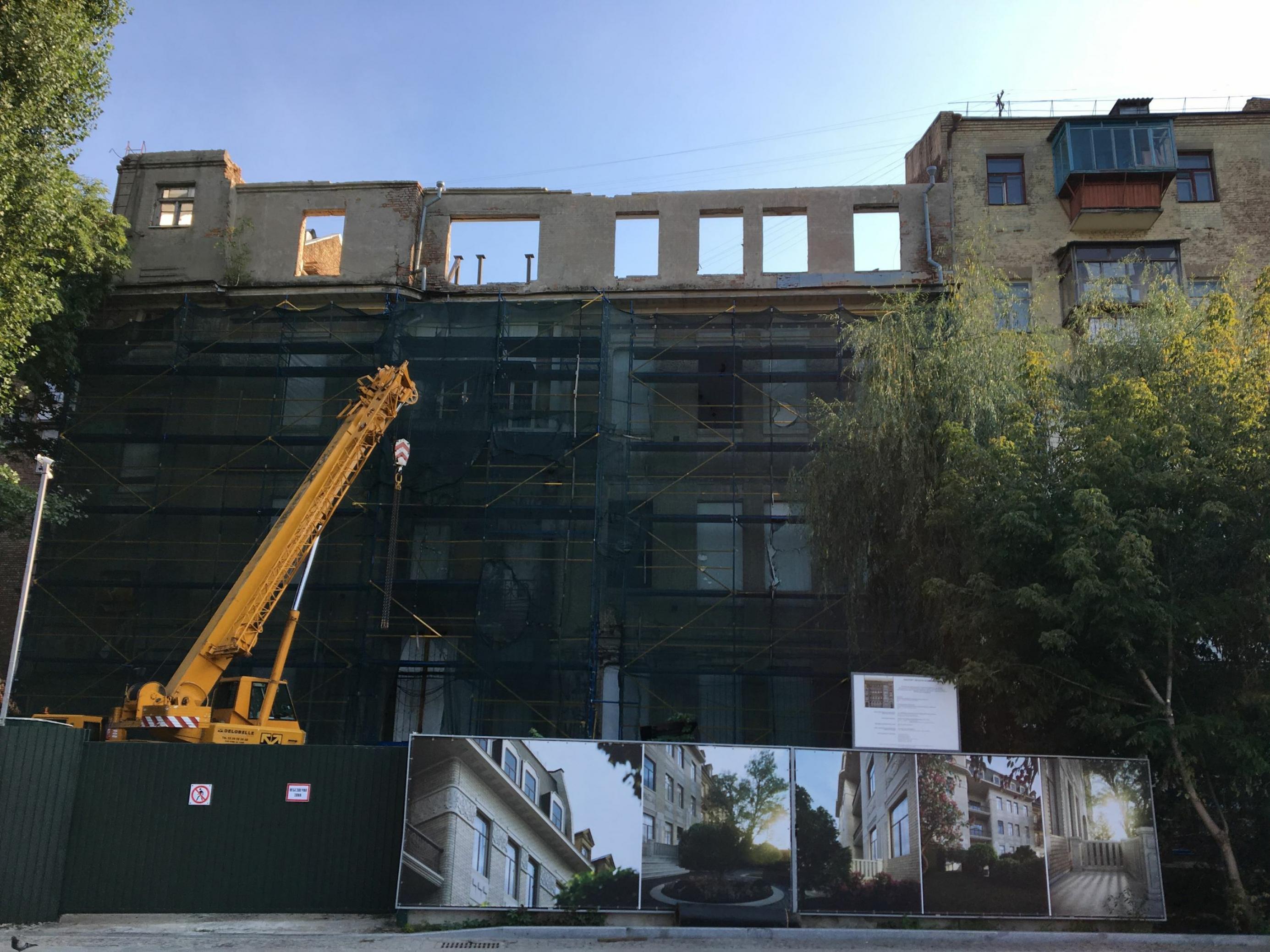Mit HIlfe eines Baufahrzeugs wird ein marodes Gebäude in der ukrainischen Hauptstadt Kiew saniert. Plakate zeigen, wie das Haus später aussehen soll.