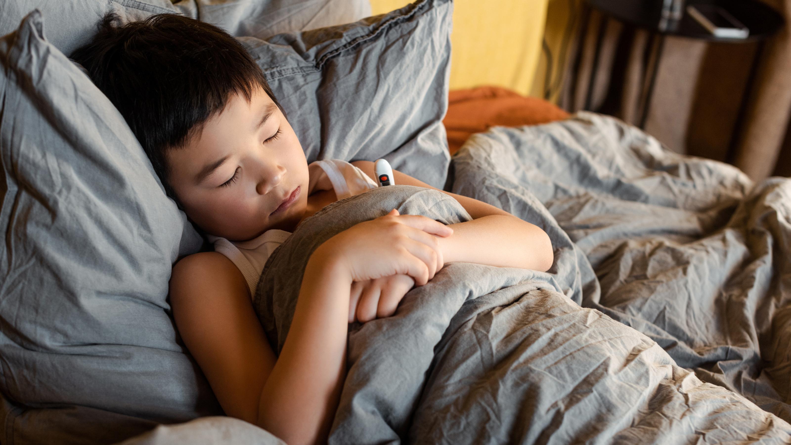 Ein etwa achtjähriger Junge liegt krank mit geschlossenen Augen im Bett.