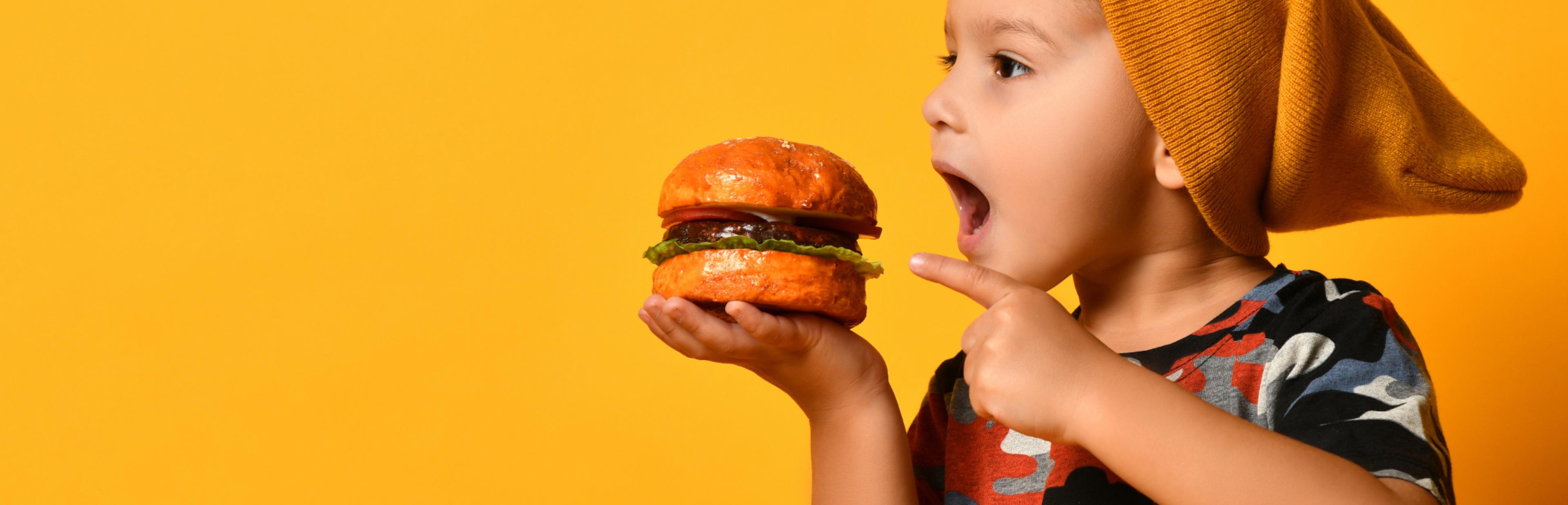 Kleines Kind zeigt auf Burger in seiner Hand