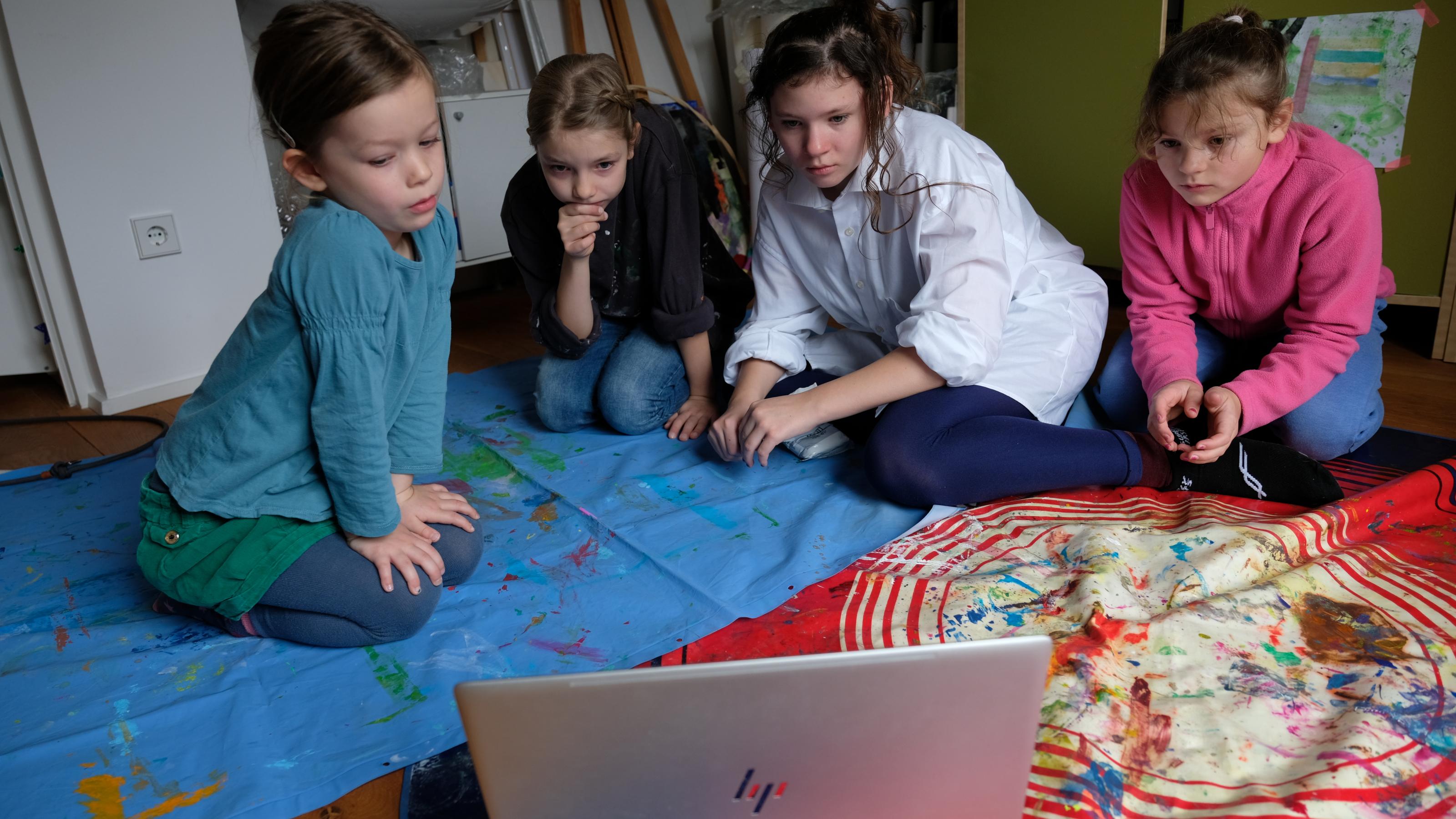 Vier Mädchen von fünf bis zwölf Jahren sitzen vor einem Notebook auf dem Boden und gucken im Internet ein Video. Die Kunstsammlung NRW erklärt auf YouTube für Kinder, wie einzelne Künstler gearbeitet haben.
