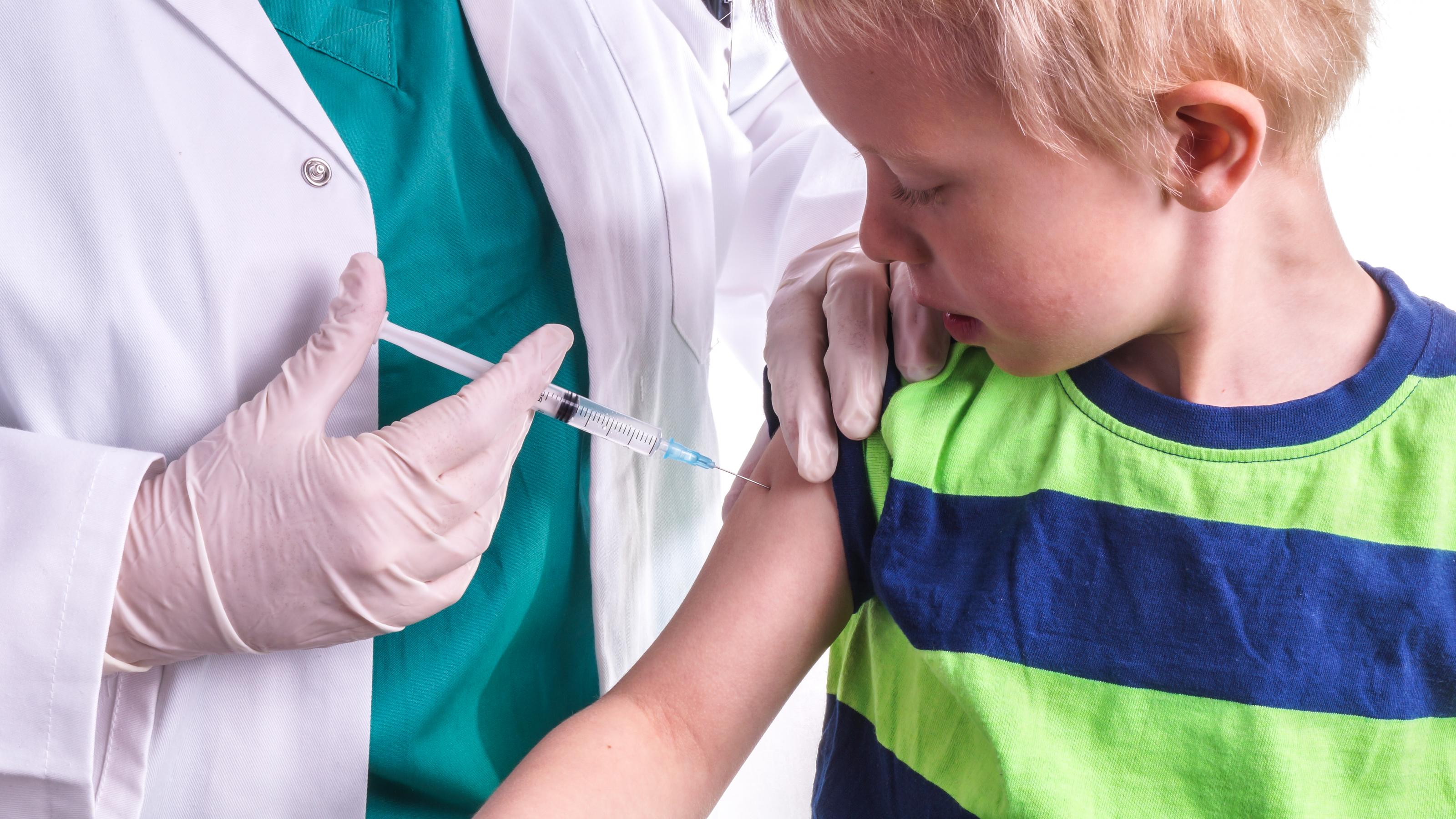 A young boy gets an injection with a syringe in his upper arm.