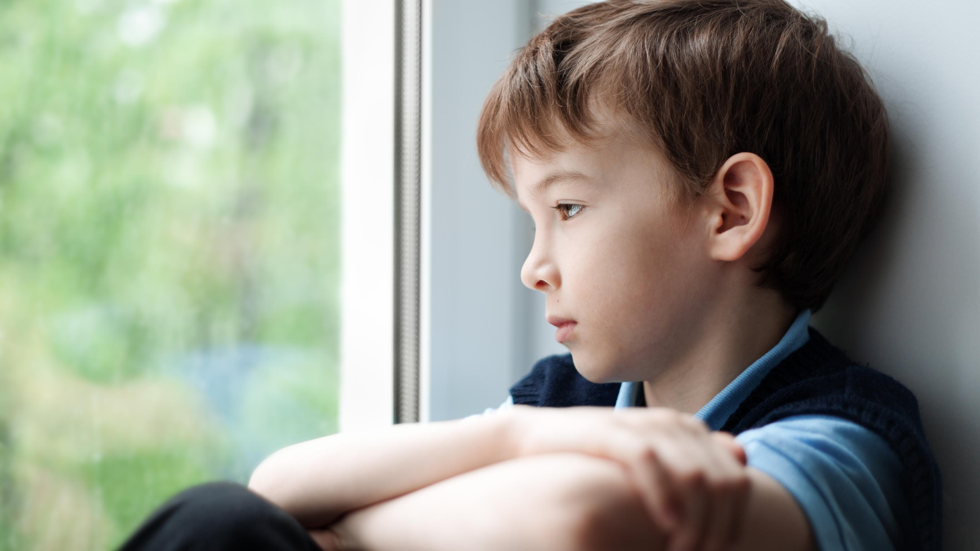 Ein Junge schaut traurig aus dem Fenster, Symbolbild für Kinderarmut, die sich nur schlecht fotografieren lässt.