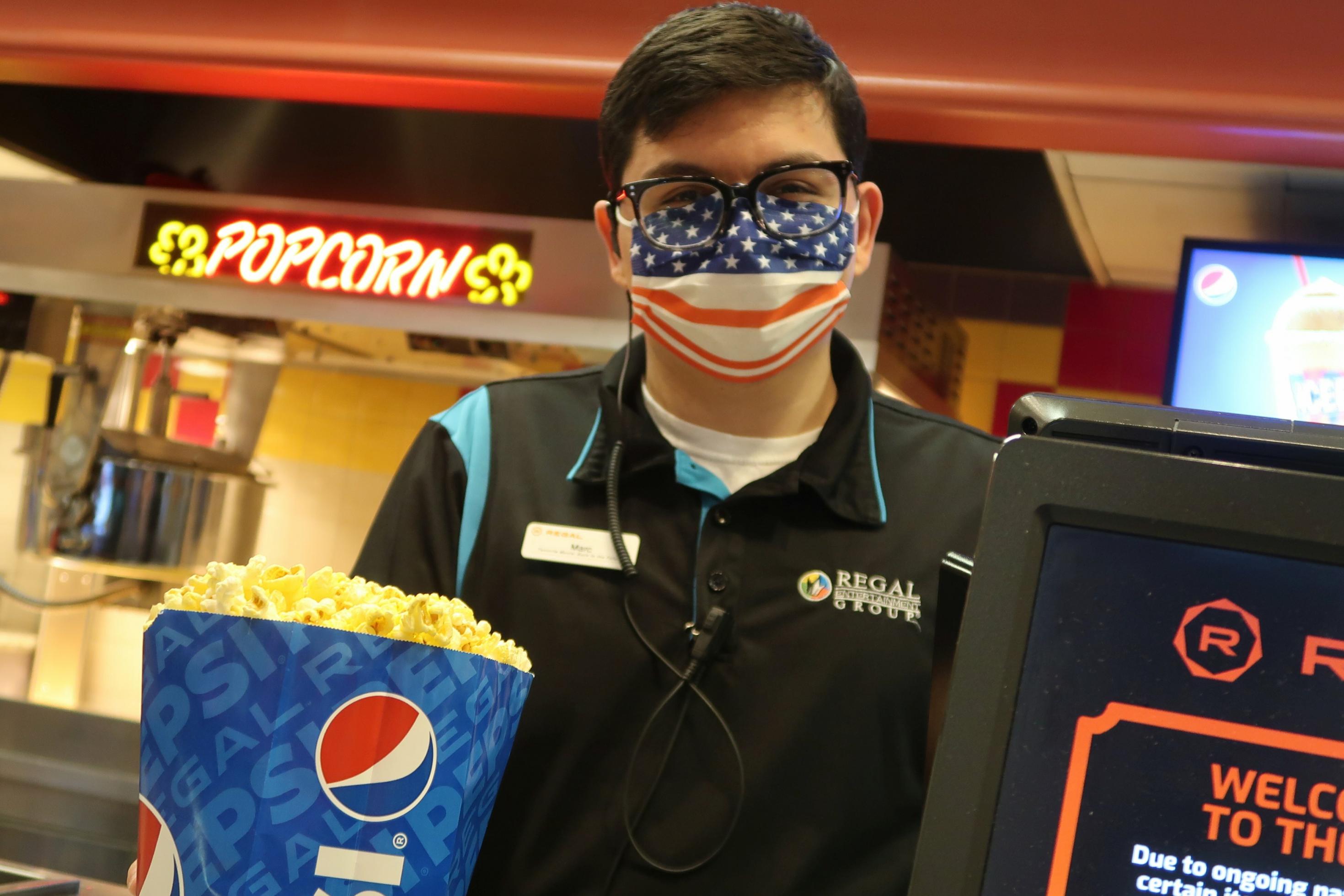 Ein Verkäufer, der eine Maske trägt, überreicht im Kino eine Tüte Popcorn.