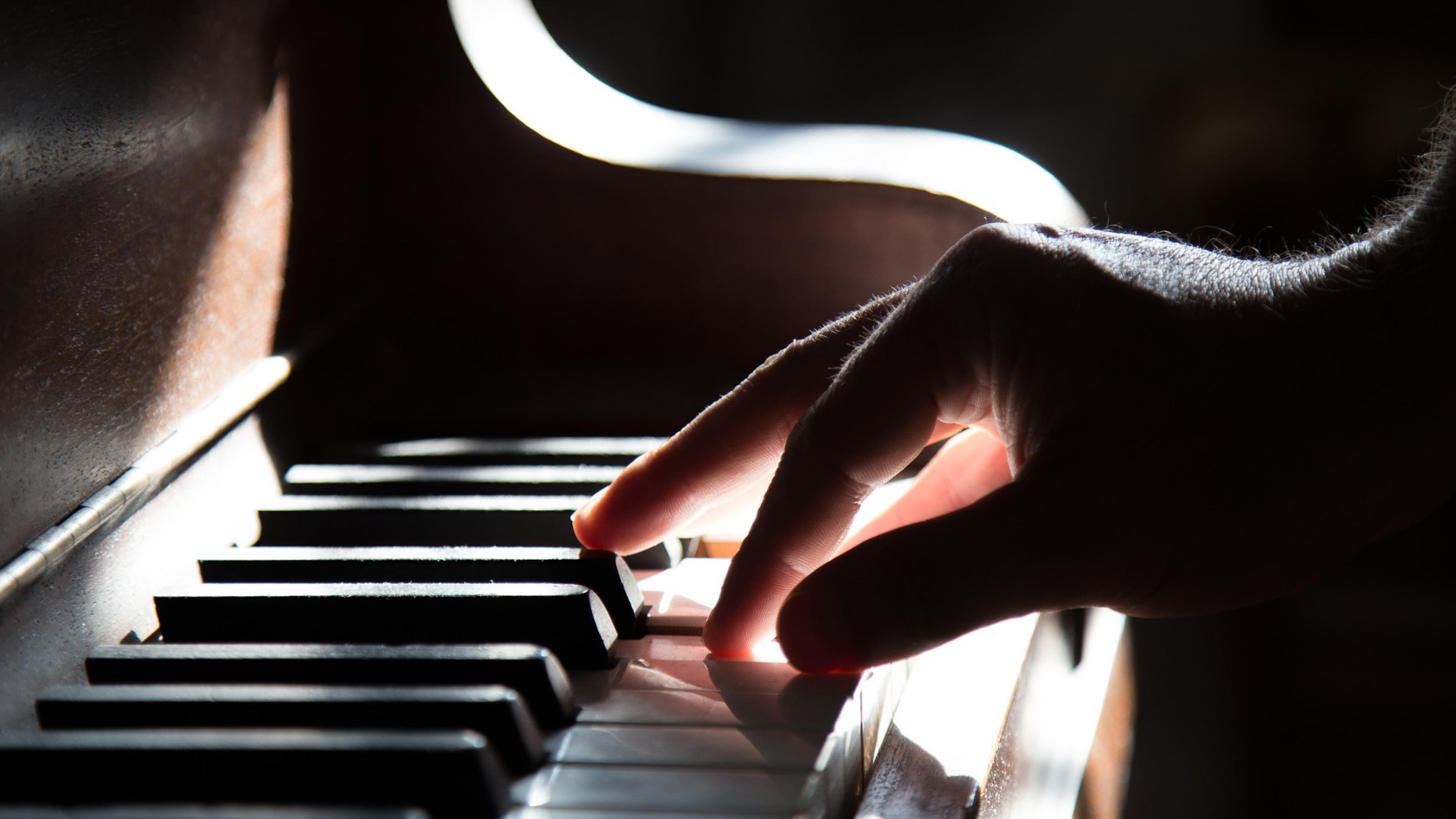 Die Hand eines Mannes spielt sanft die Tasten eine Klaviers.