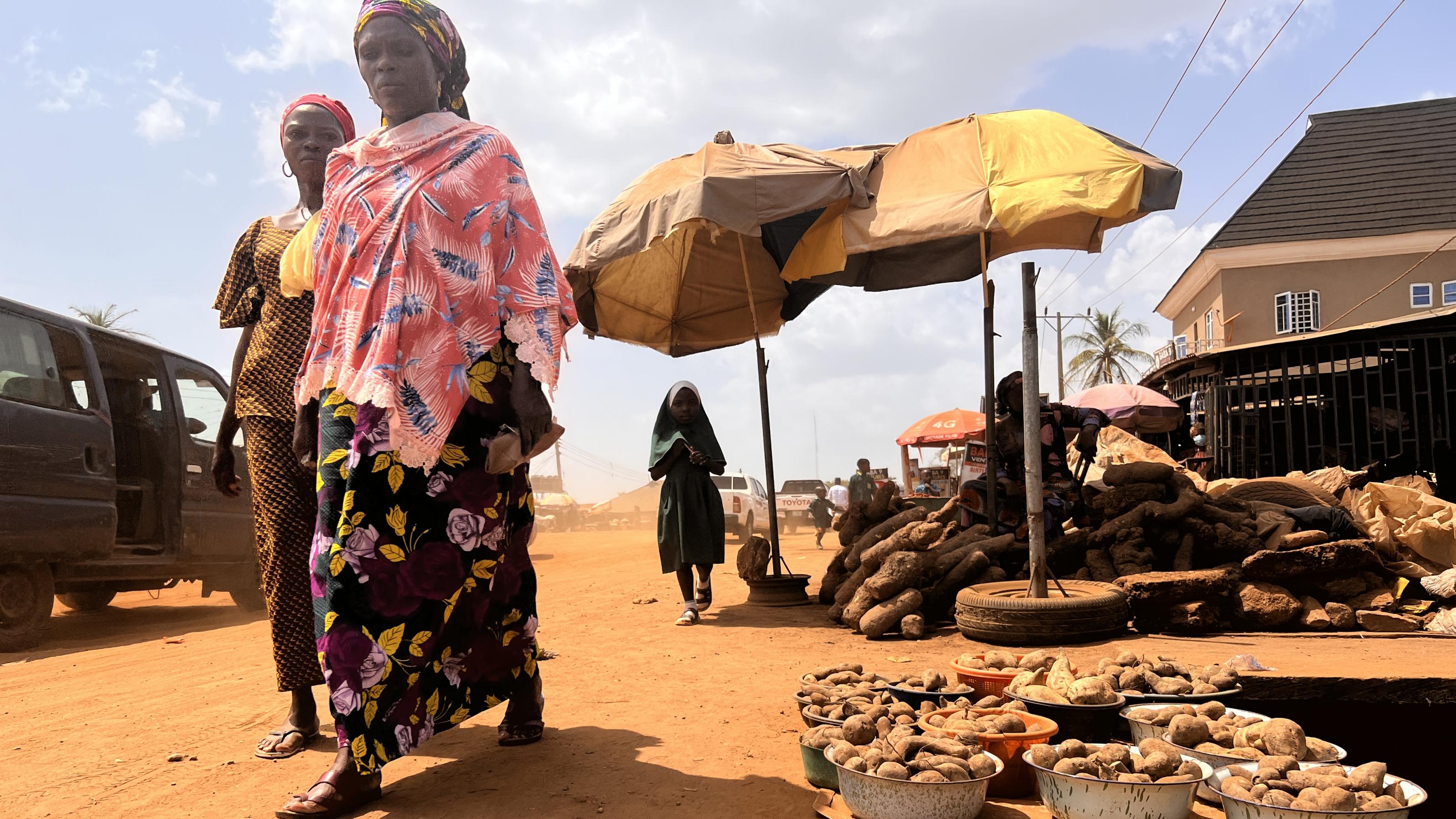 Zwei Frauen mit Kopftüchern gehen an kleinen Schalen mit Knollen vorbei, die von Kleinbauern in Kwara, Nigeria, verkauft werden.
