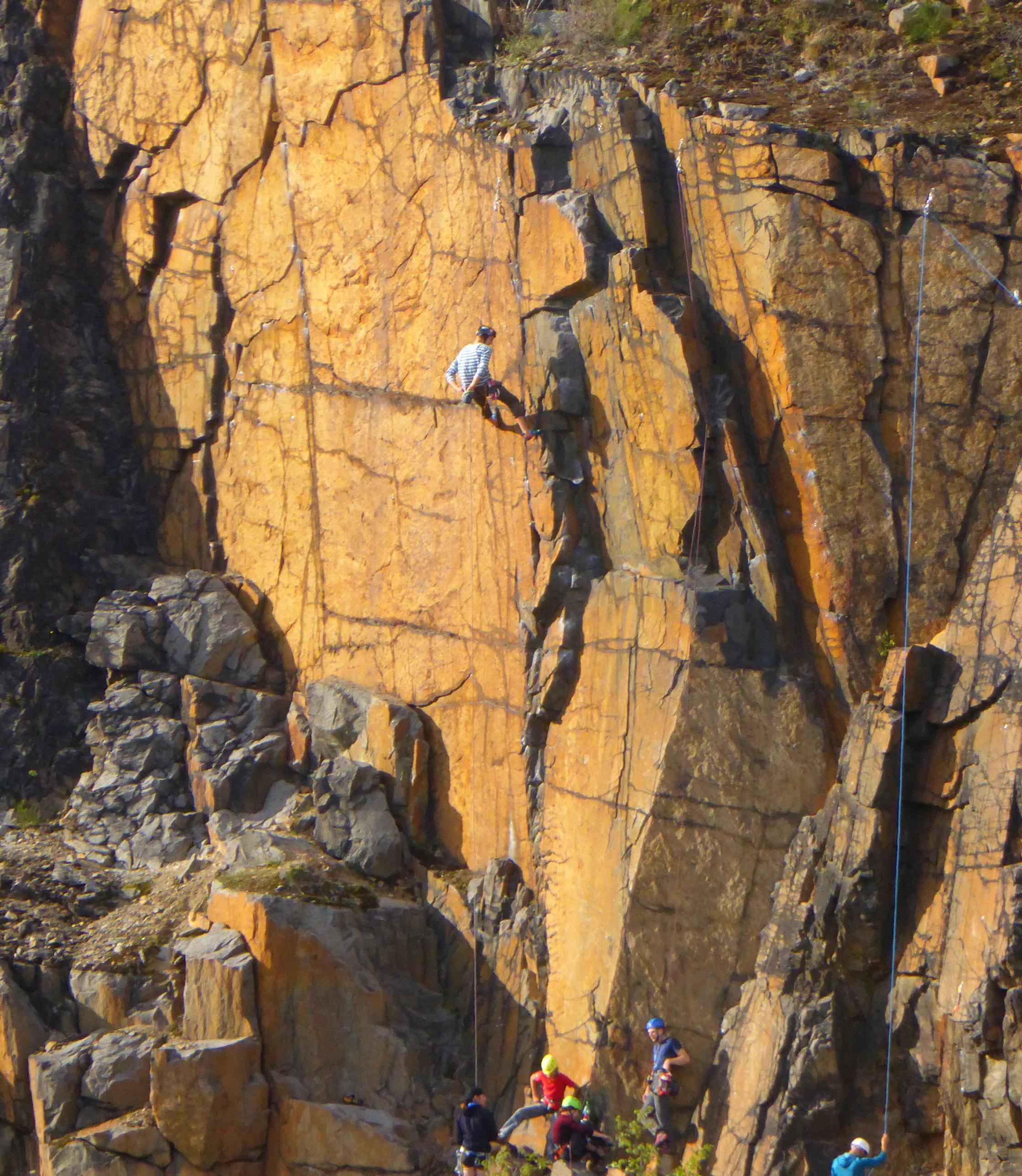 Kletternde Menschen an einer schroffen, rotgelben Felswand.