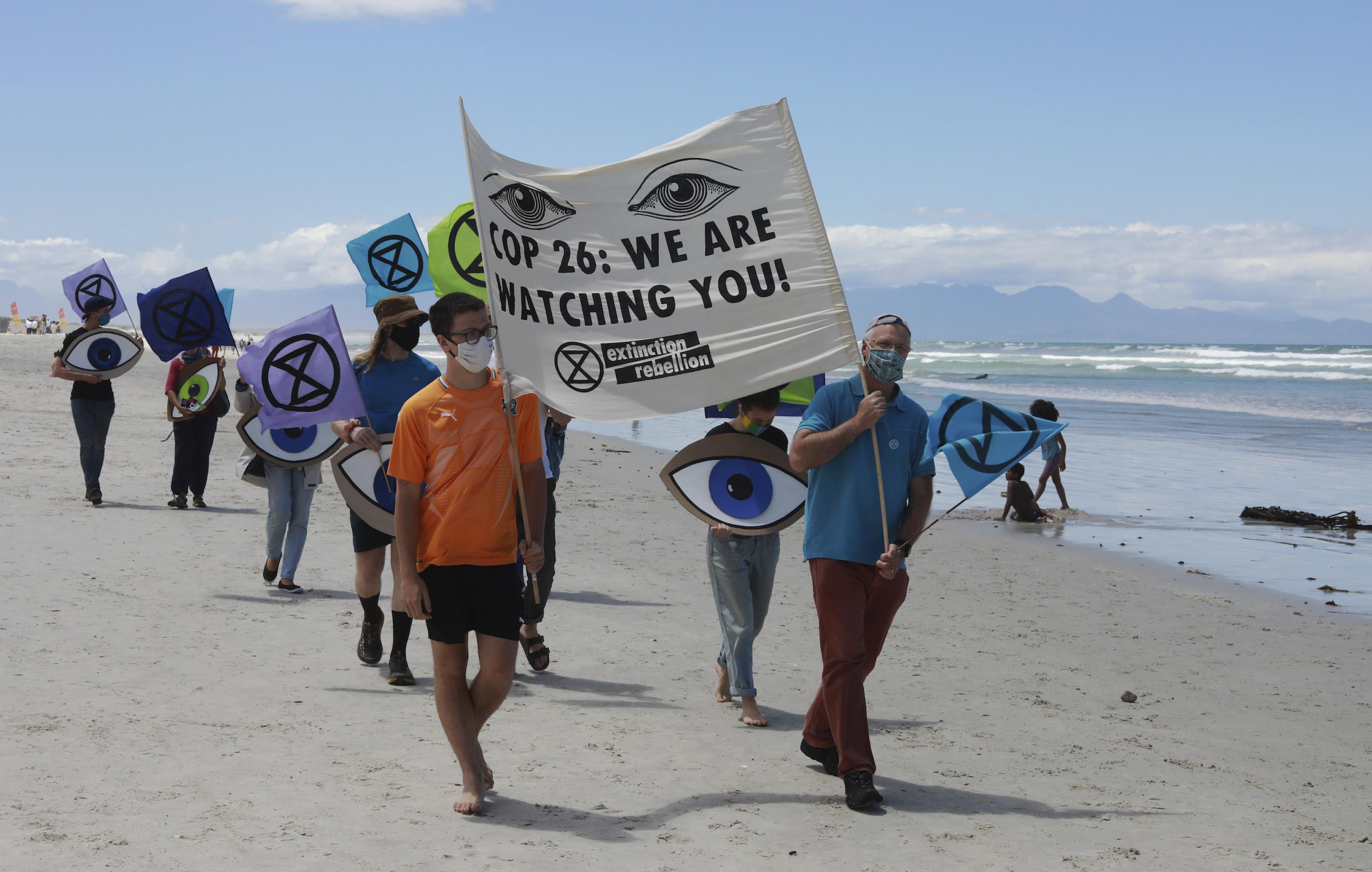 Demonstranten am Strand in Südafrika tragen ein Schild mit der Aufschrift „COP26 wir beobachten dich“.