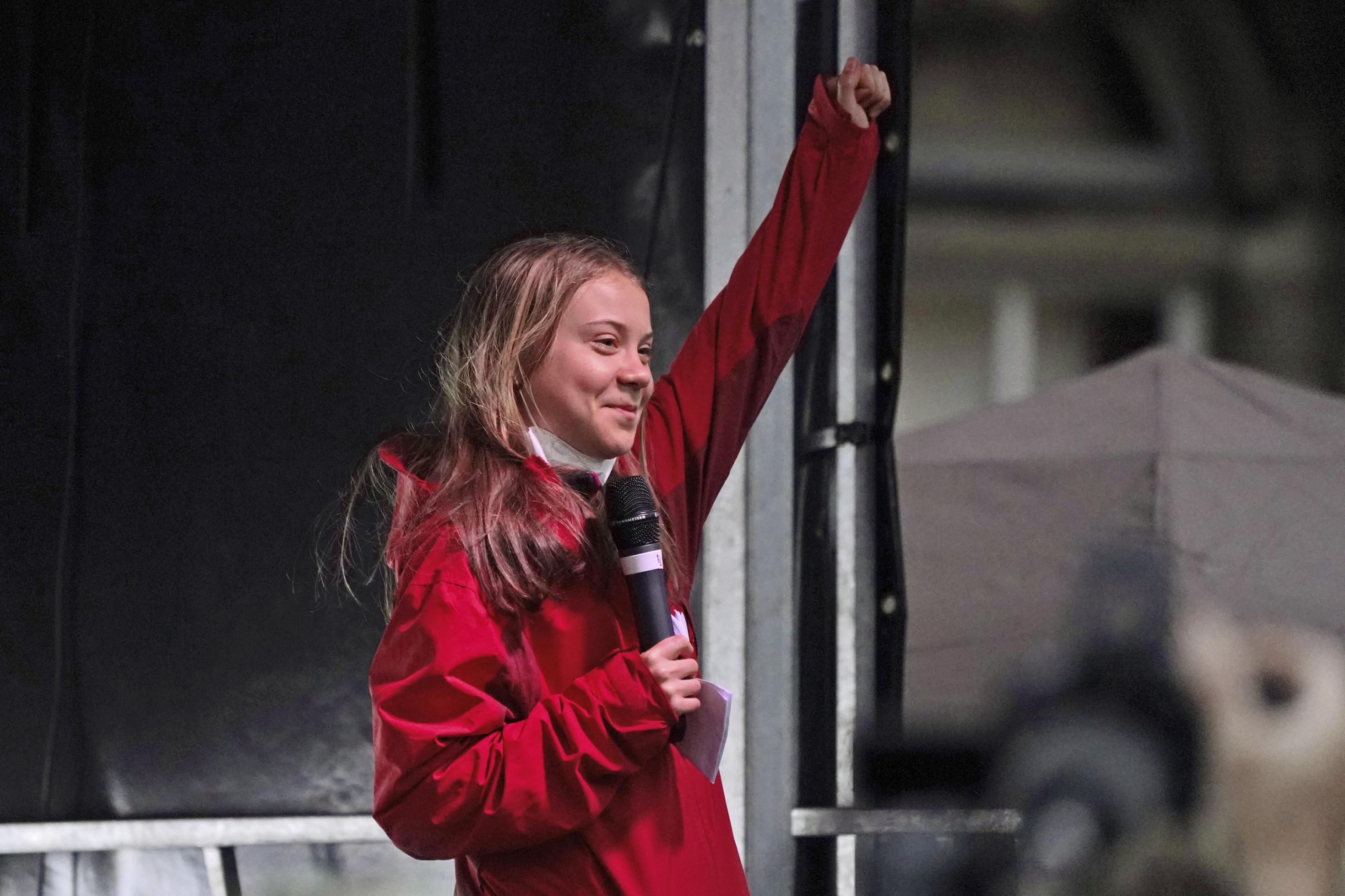 Great Thunberg mit geballter Faust auf einer Bühne, sie lächelt.