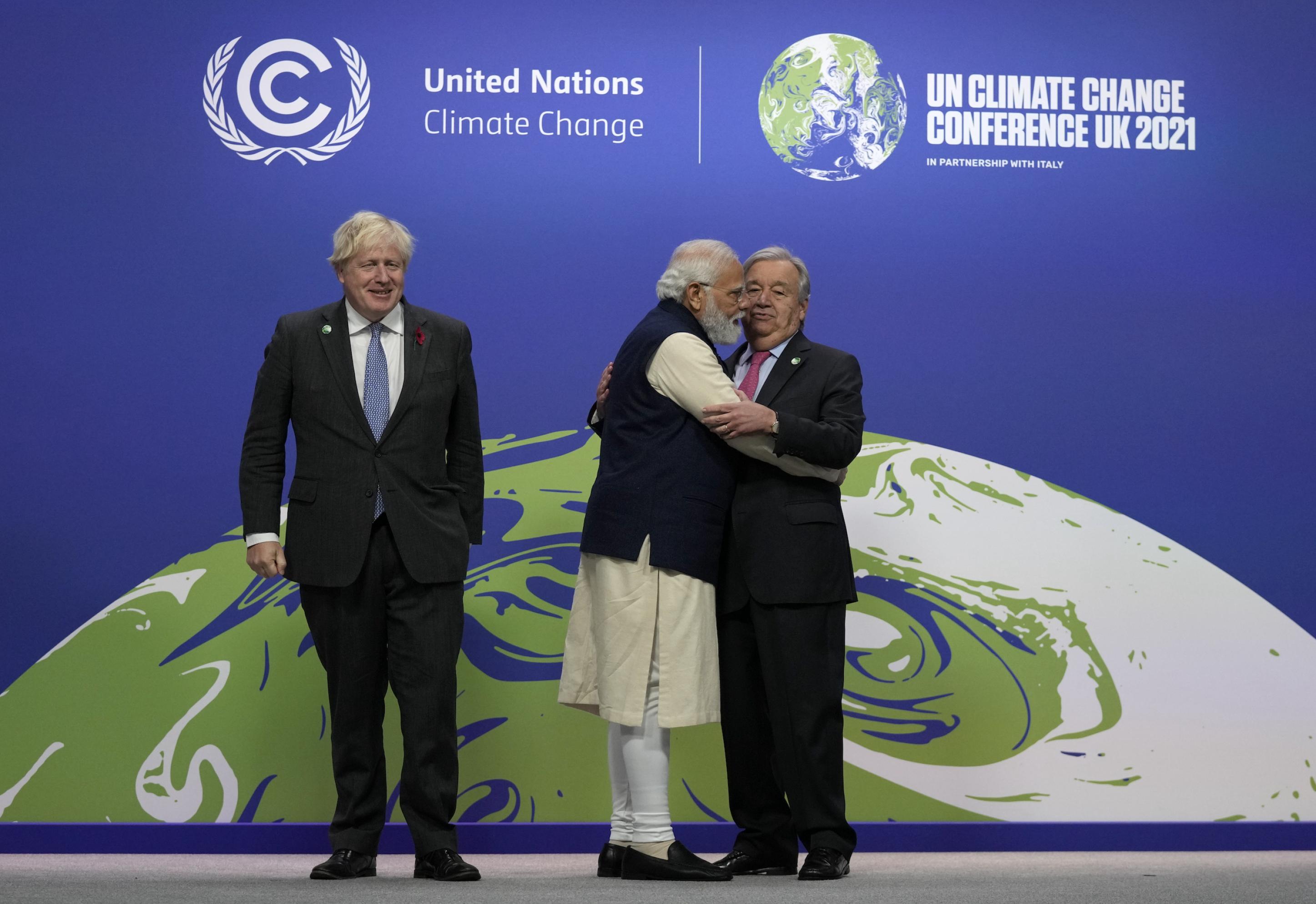 Boris Johnson, UN-Generalsekretär Antonio Guterres und der indische Premier Narendra Modi auf der Bühne. Modi umarmt Guterres, der davon überrascht zu sein scheint.