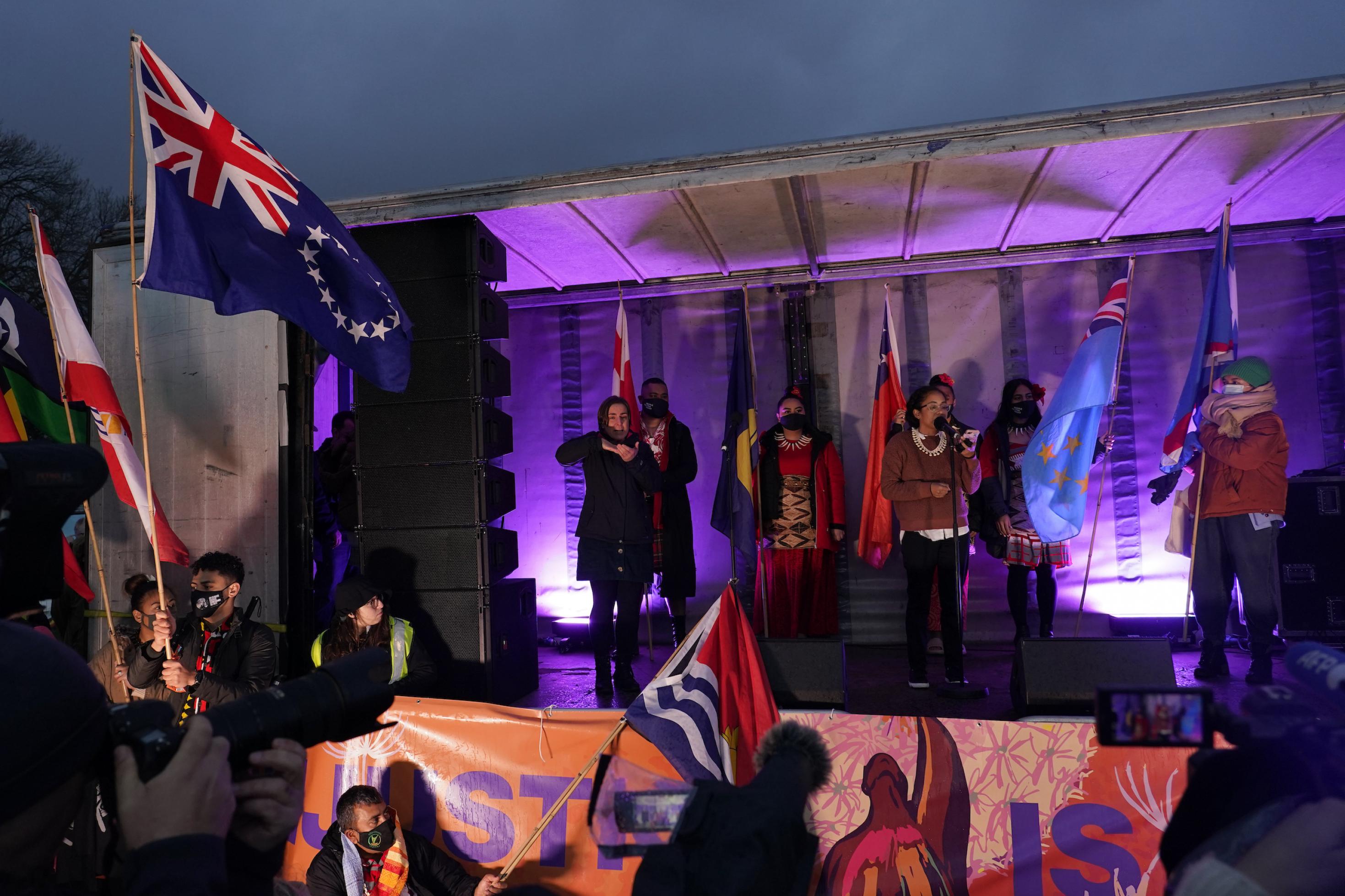 Frauen stehen auf einer Bühne, vor ihnen werden Fahnen von Pazifikstaaten geschwenkt.