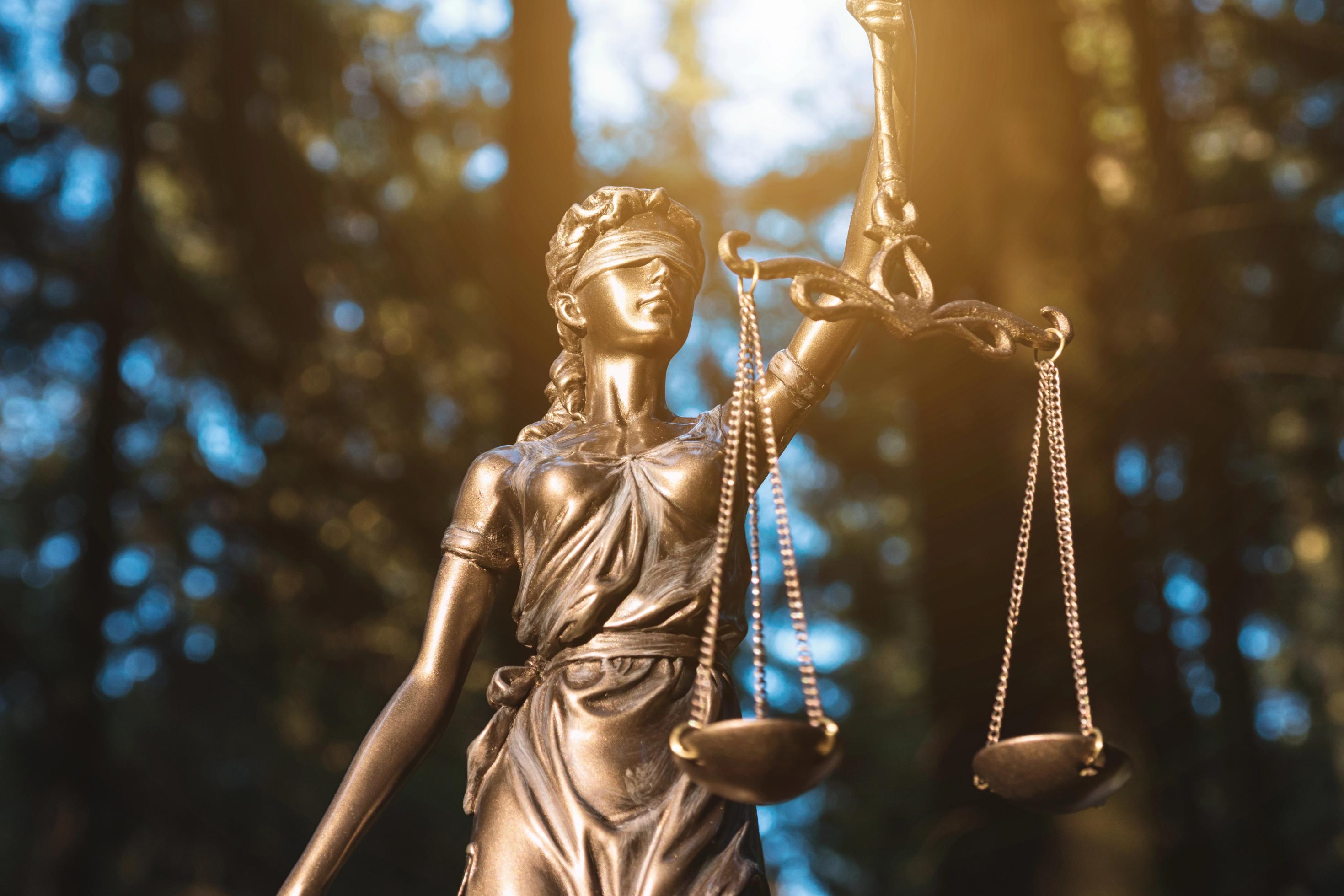 Die Lady Justice (Frau mit verbundenen Augen und Waage in der Hand) im Wald