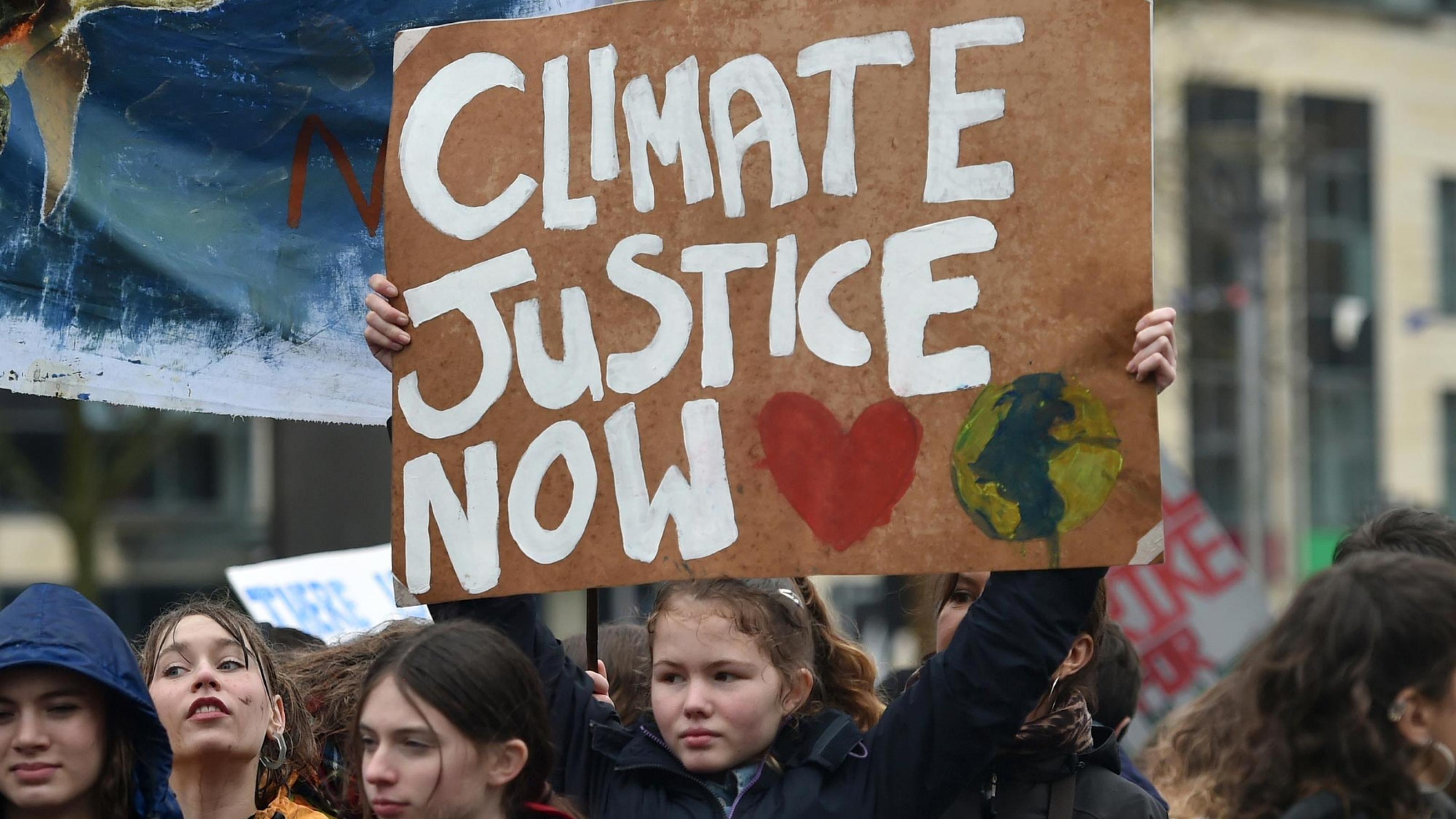 Demonstierende Menschen mit einem Plakat, auf dem „Climate Justice Now“ steht.