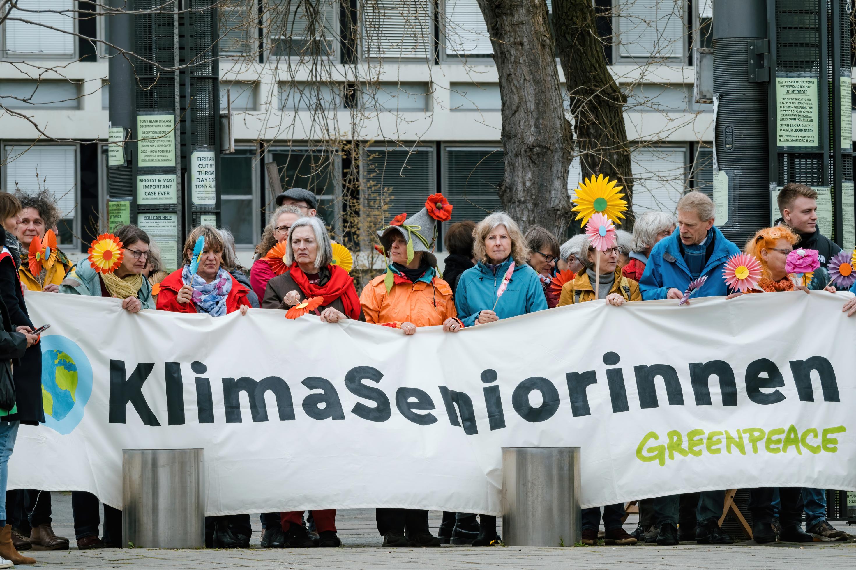 Totale der KlimaSeniorinnen mit weißem Banner in der Hand. Darauf stehen die Schriftzüge KlimaSeniorinnen sowie Greenpeace.