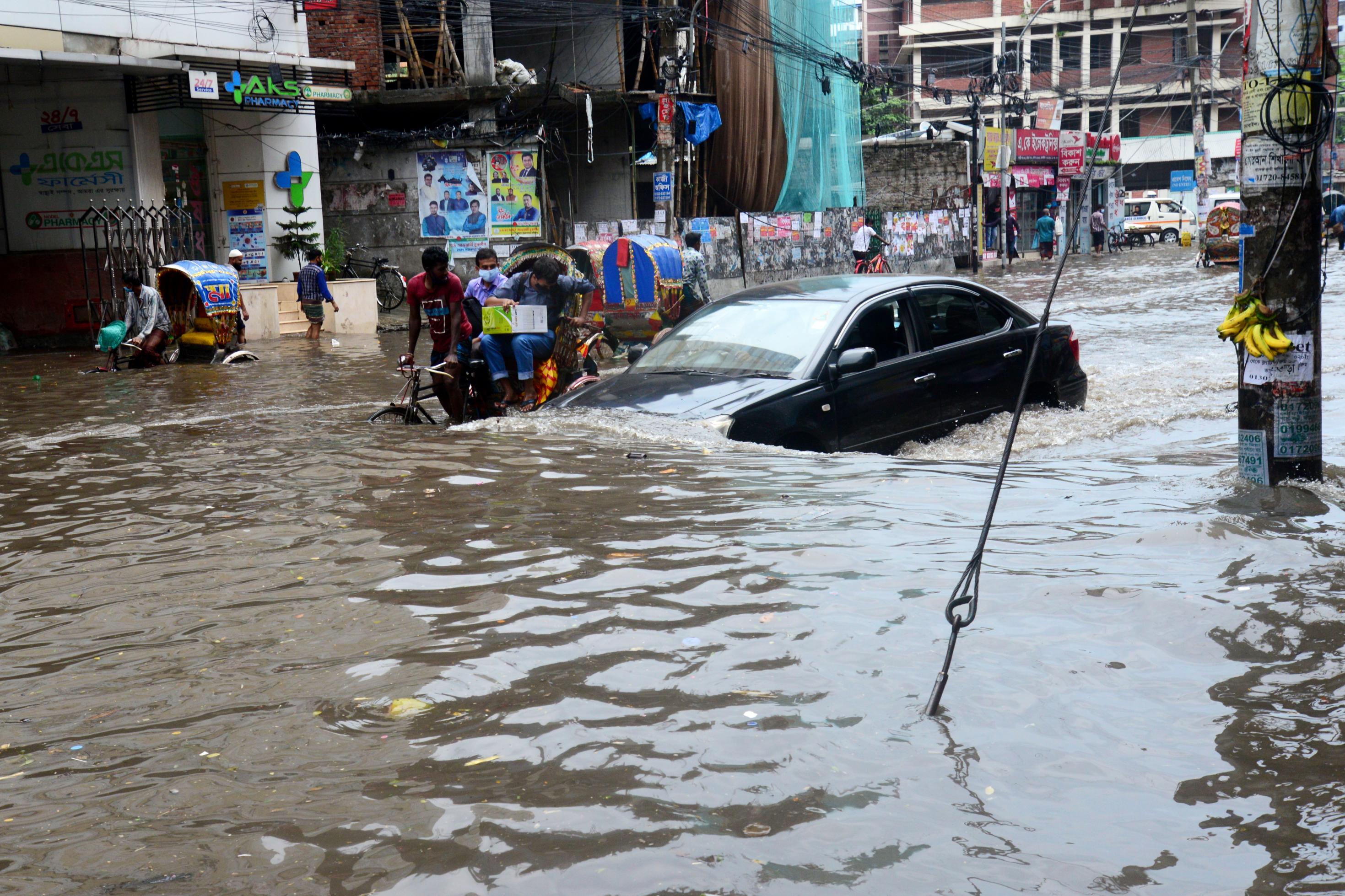 Eine überflutete Straße in Dhaka, Bangladesch, 2020. Autos, Radfahrer, Fußgänger kämpfen sich durch die Wassermassen.