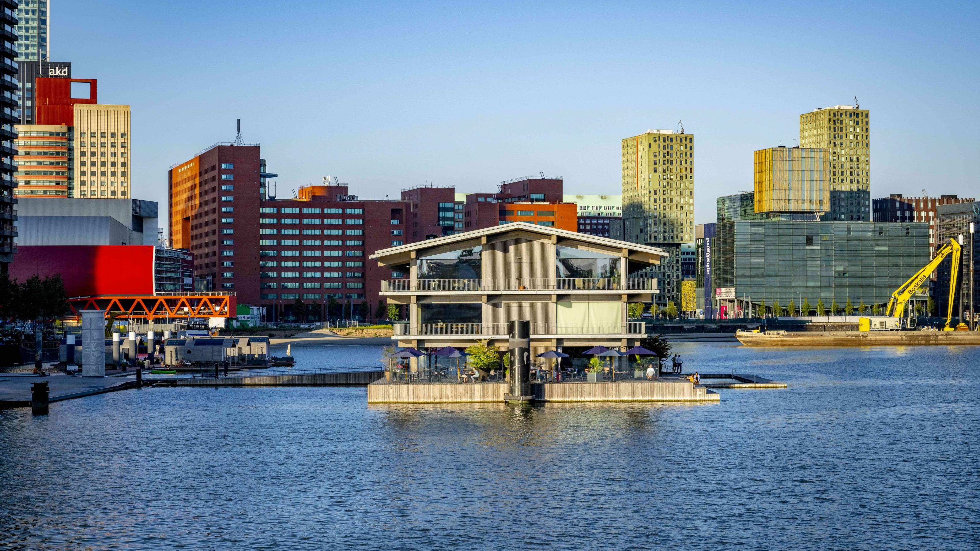 Hochhäuser umgeben ein mehrstöckiges Gebäude mit Cafés, das in einem Hafenbecken schwimmt: Es ist das größte im Wasser treibende Bürogebäude der Welt.