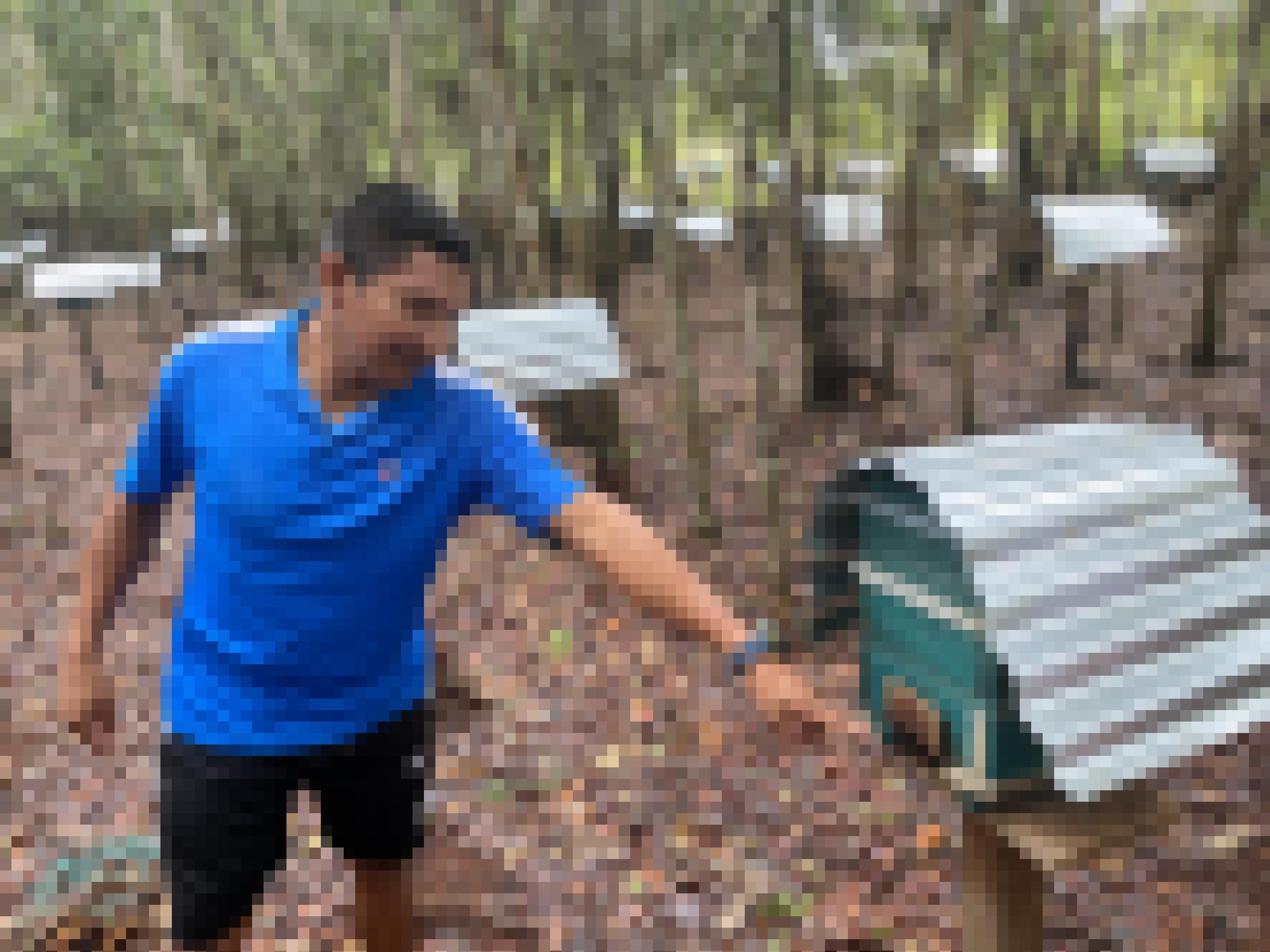 Fabio Pérez im blauen Shirt steht umgeben von Briefkasten-ähnlichen Bienenstöcken im Urwald.