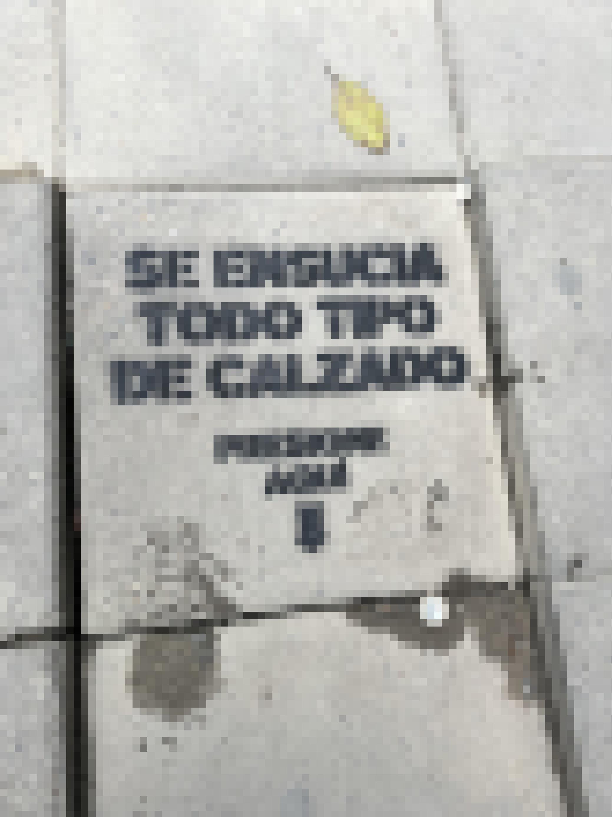 Auf eine grauen schlichten Bodenplatte eines Gehwegs ist auf Spanisch dieser Text mit einer Schablone gesprüht. Am Ende zeigt ein Pfeil auf die Stelle, auf die man treten soll (was auch an zwei feuchten echten Schuhabdrücken zu erkennen ist).