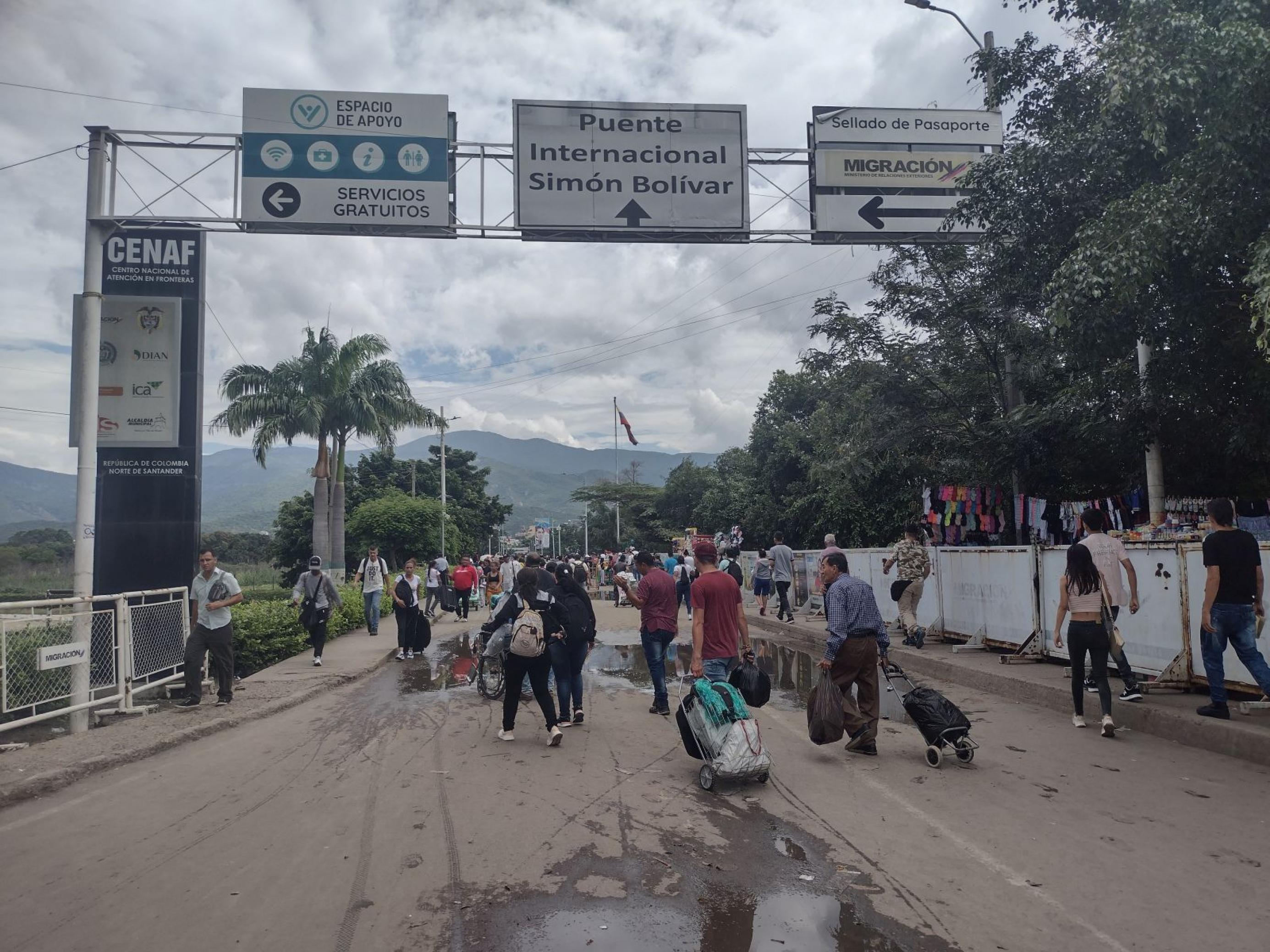 Strasse mit Schild oben: internationale Brücke Simon Bolivar. Menschen mit Rollkoffern laufen in beide Richtungen