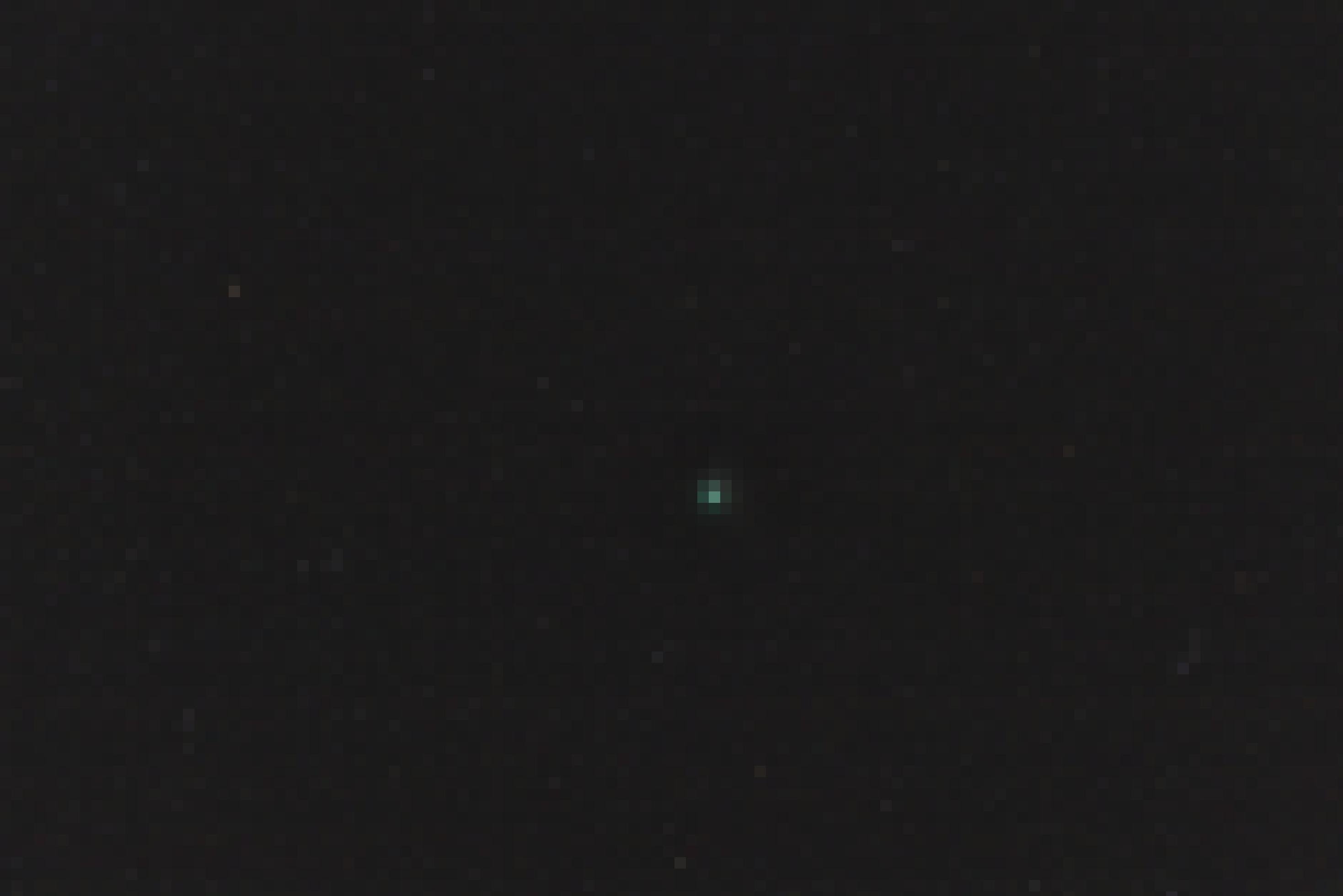 In einem Foto des Sternenhimmels ist als hellstes Objekt in der Bildmitte ein Komet zu sehen, dessen helles, sternartiges Zentrum von einer diffusen, grünen Hülle umgeben ist.
