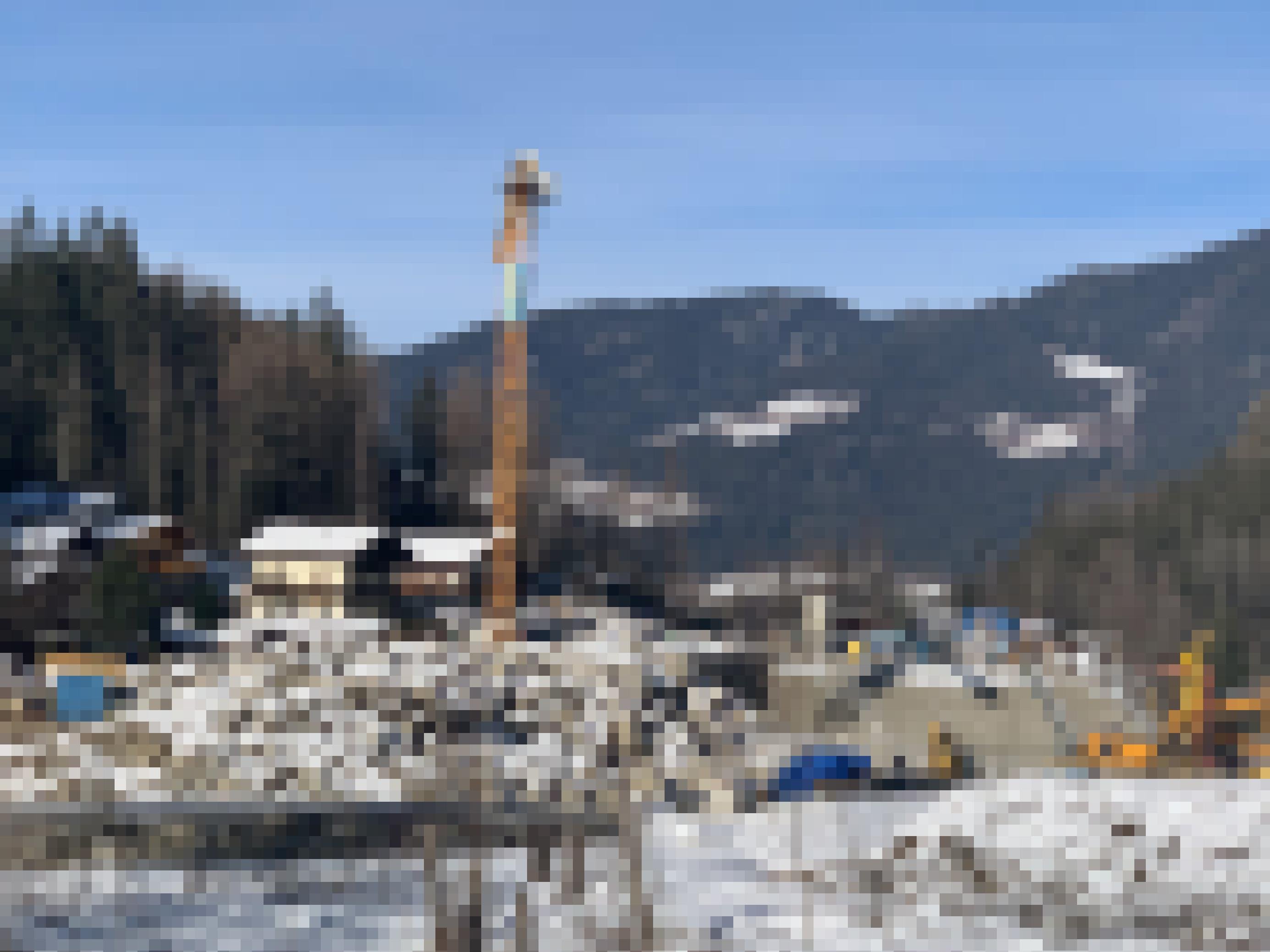 Landschaft an Gebirgsbach mit Baukran, Betonwand und einem großen Haufen Steinen