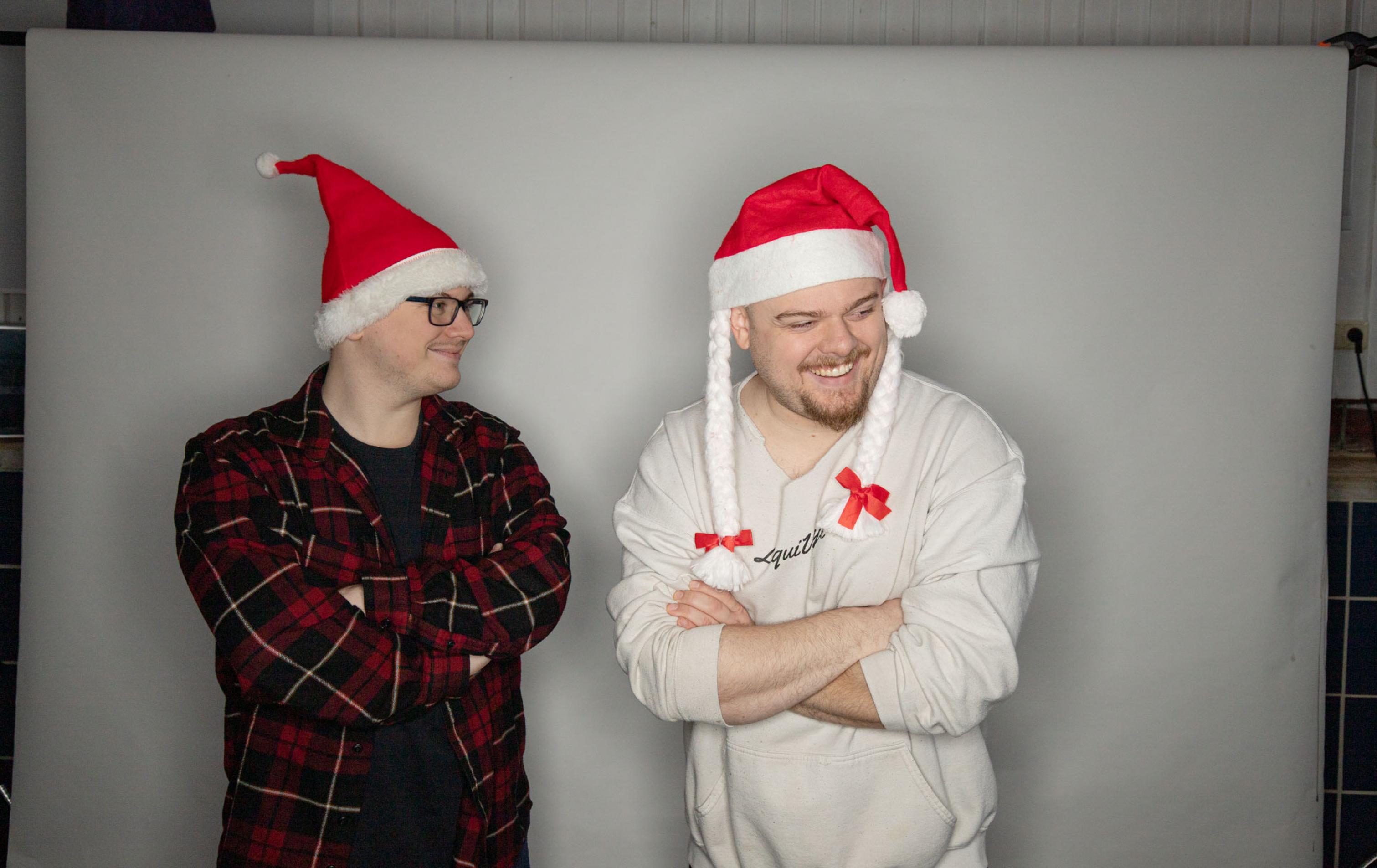 Zwei Brüder tragen eine Weihnachtsmuetze im Fotostudio und lachen