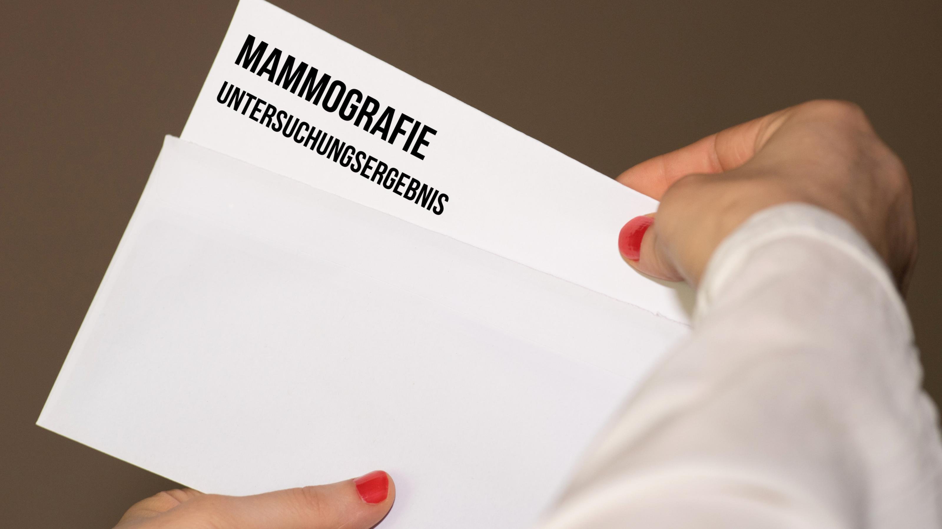 Eine Frau öffnet einen Umschlag mit den Ergebnissen einer Mammographie-Untersuchung.