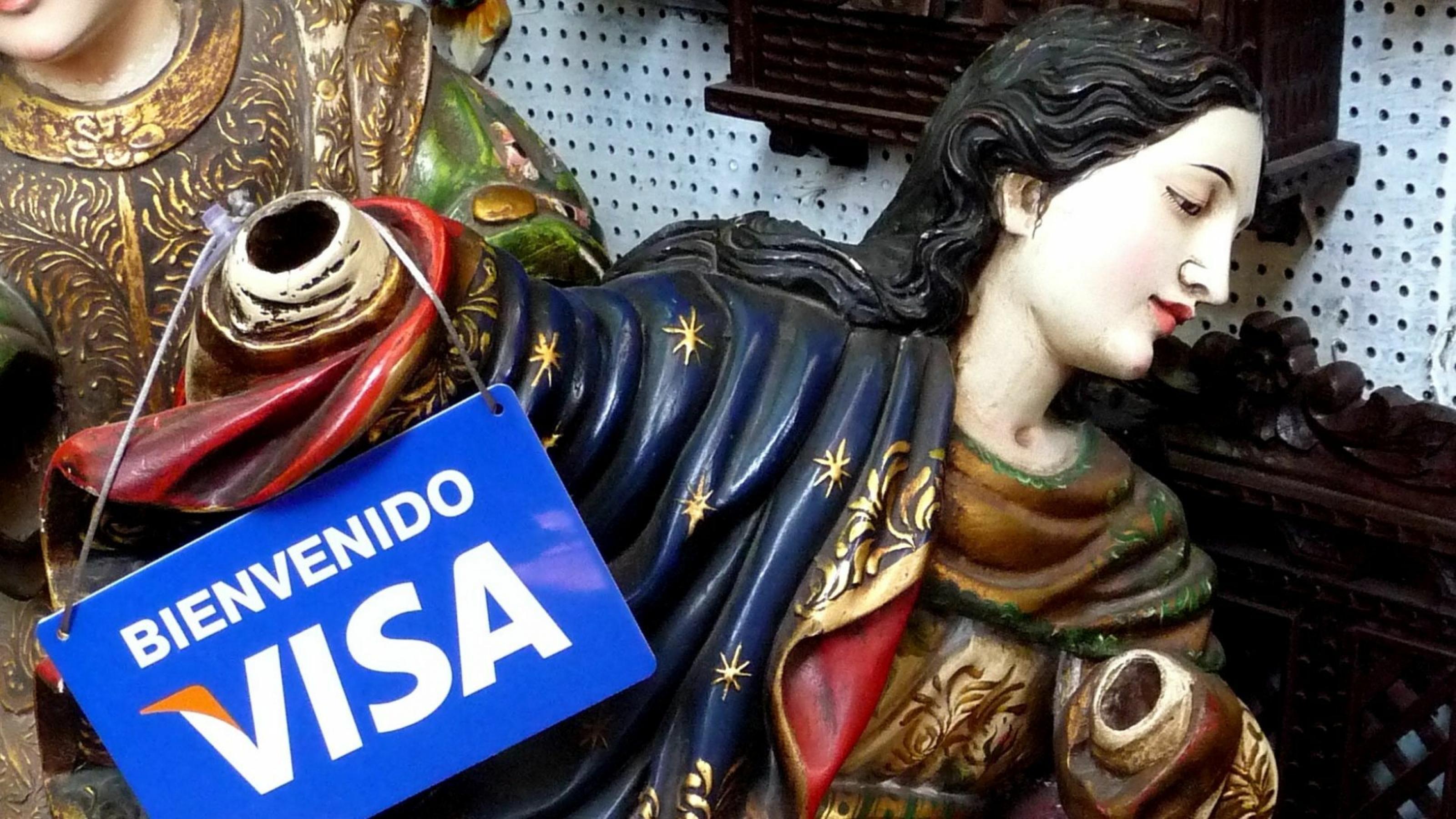 Geschnitzte und bemalte Statue des Sabinus von Spoleto, an deren Arm ein Schild hängt mit der Aufschrift „Visa willkommen.“