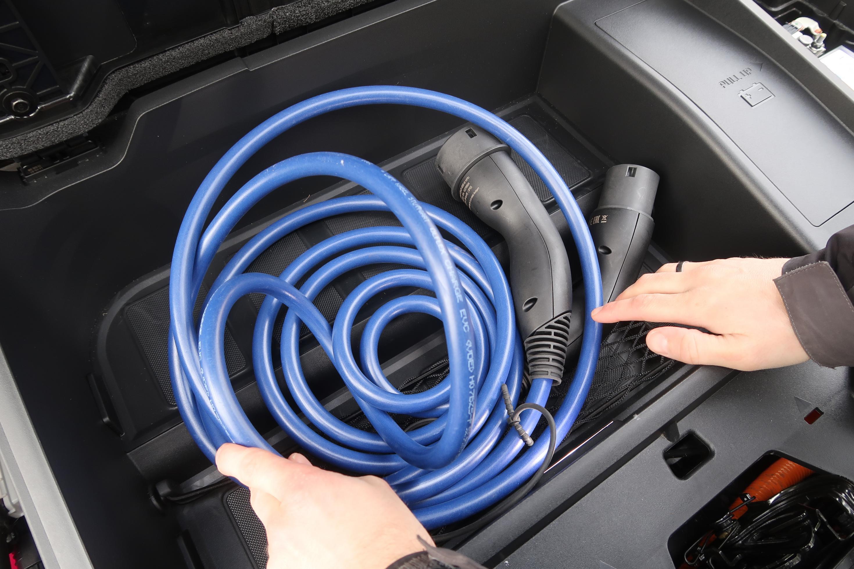 Zwei Hände verstauen ein Ladekabel im Frunk eines Elektroautos.