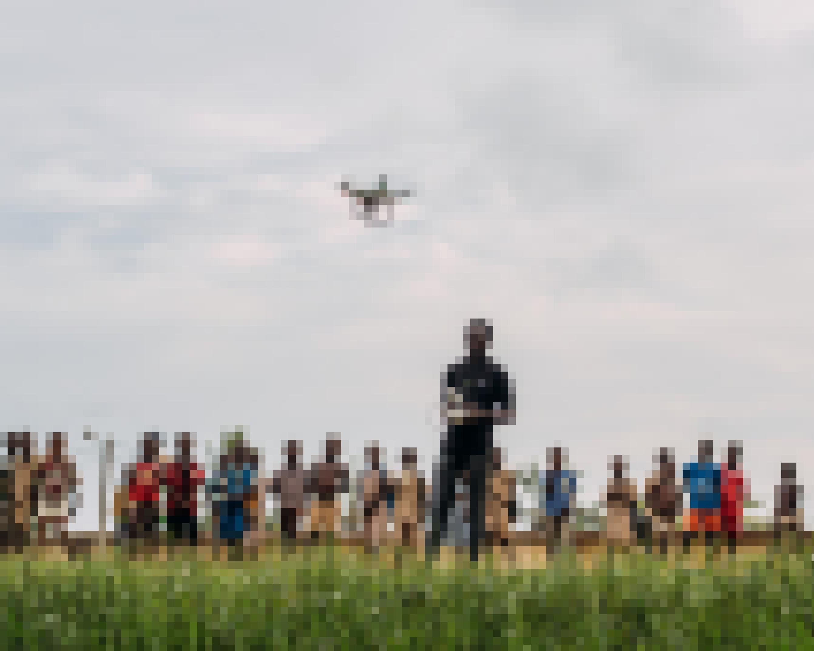 Ein Mann steuert per Fernbedienung eine Drohne. Im Hintergrund stehen einige Kinder, die die Drohne beobachten.