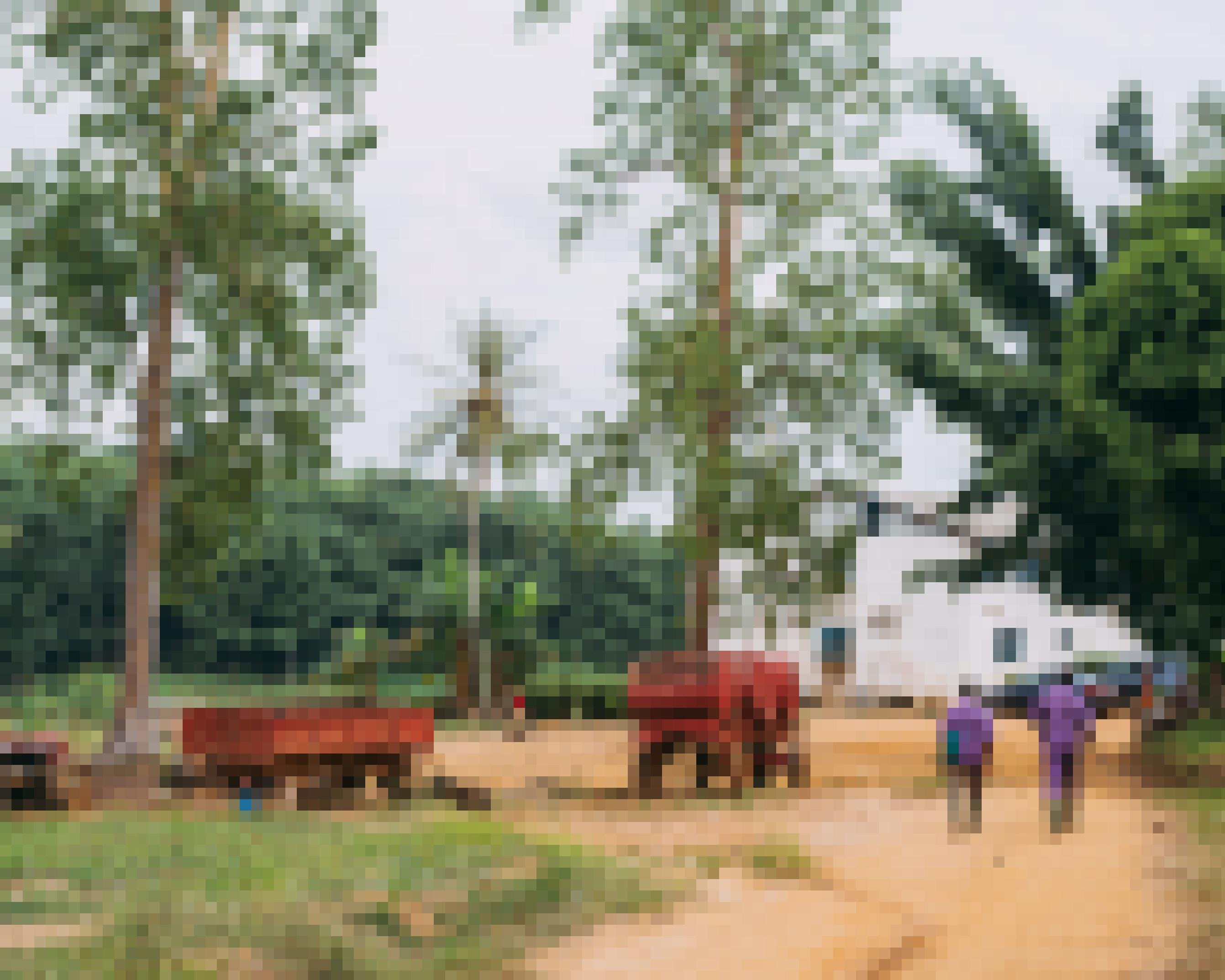 Zwei Arbeiter laufen in Richtung eines einfachen weißen Hauses.  Zwei alte rote Anhänger stehen in der Gegend rum.