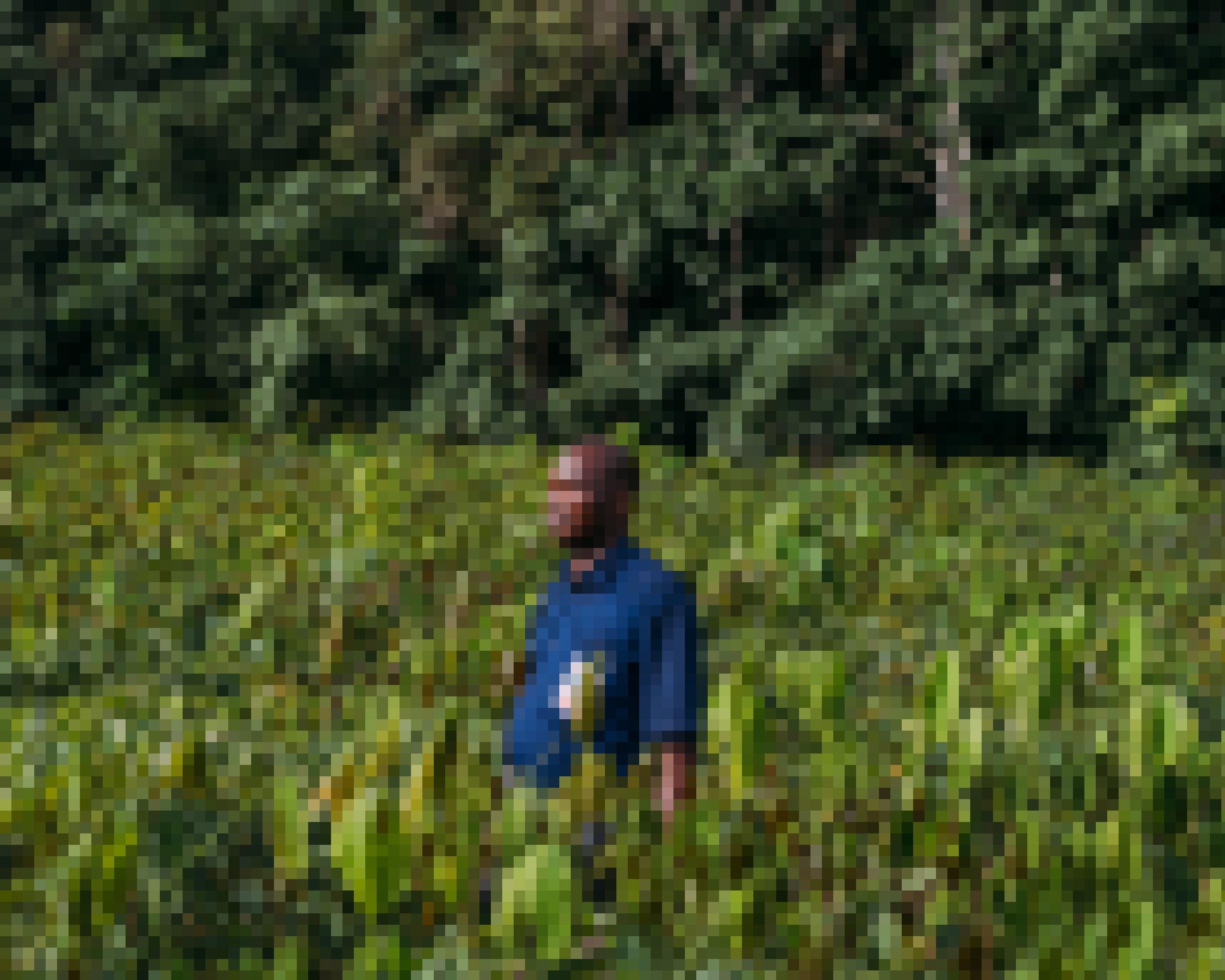 Ein afrikanischer Mann im dunkelblauen Hemd steht mit zufriedenem Gesichtsausdruck in einem Feld seiner Plantage. Sein Blick geht in die Ferne.