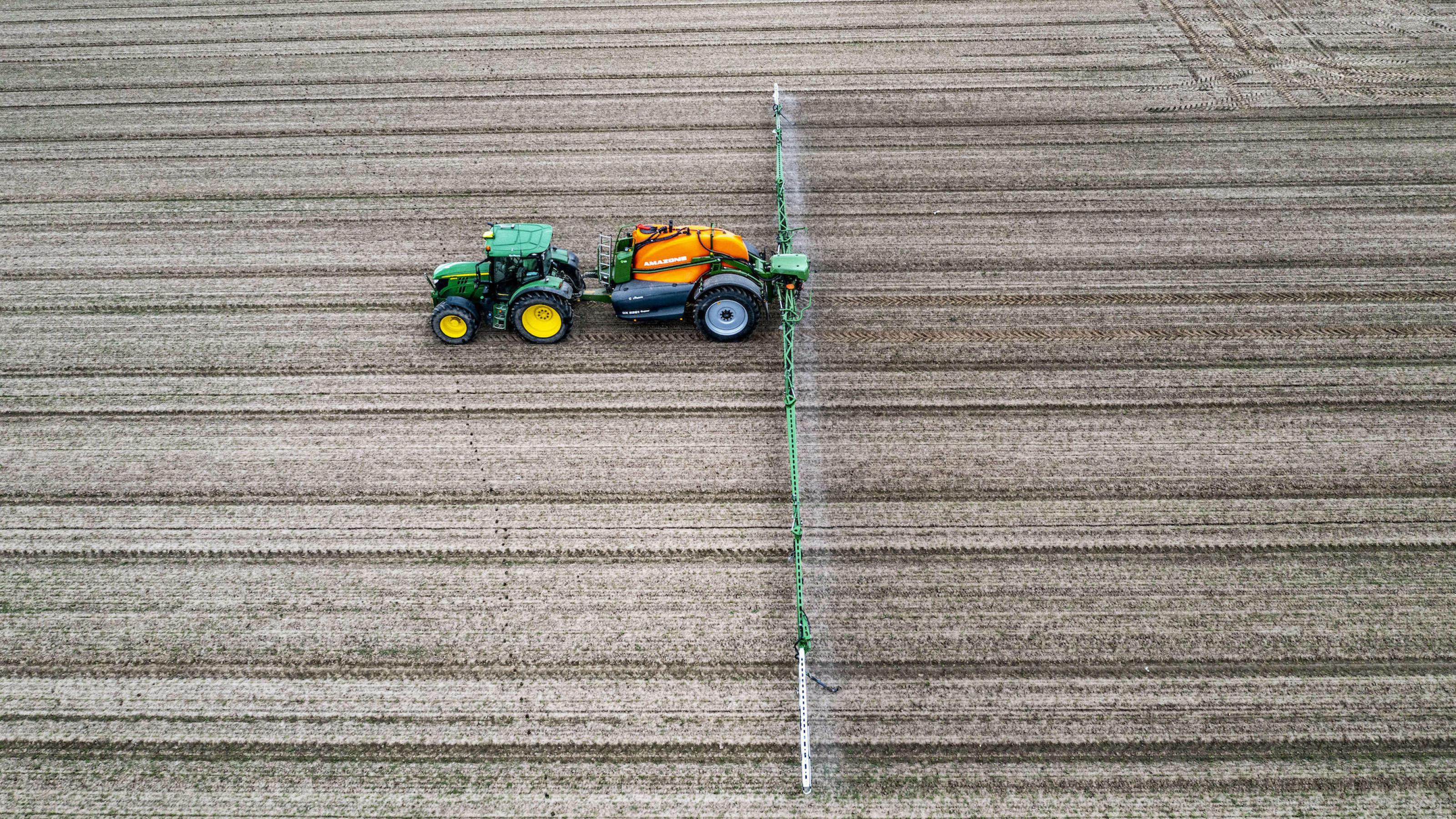 Luftaufnahme von Traktor auf barem Feld mit Sprühdüsen