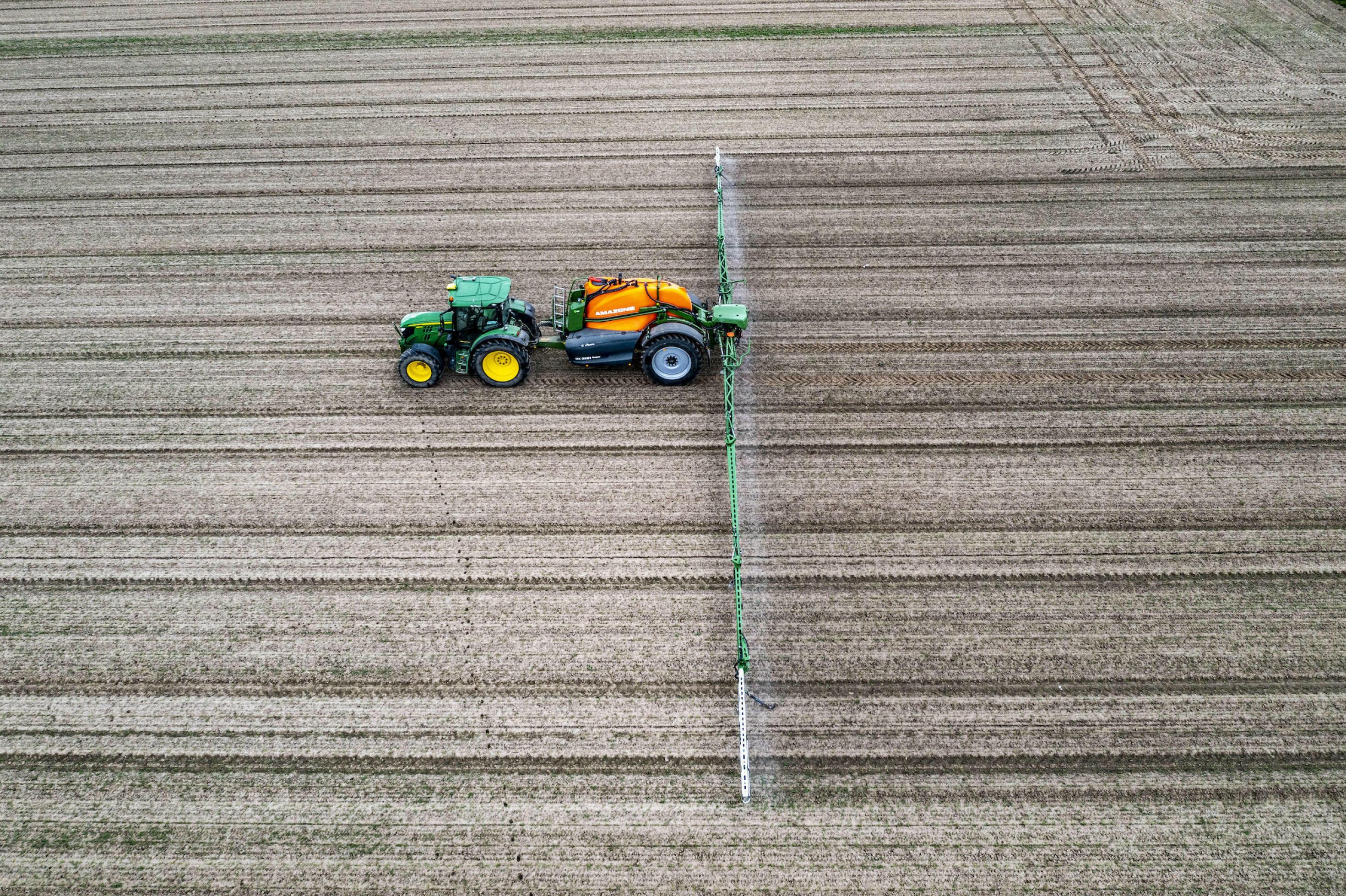 Luftaufnahme von Traktor auf barem Feld mit Sprühdüsen