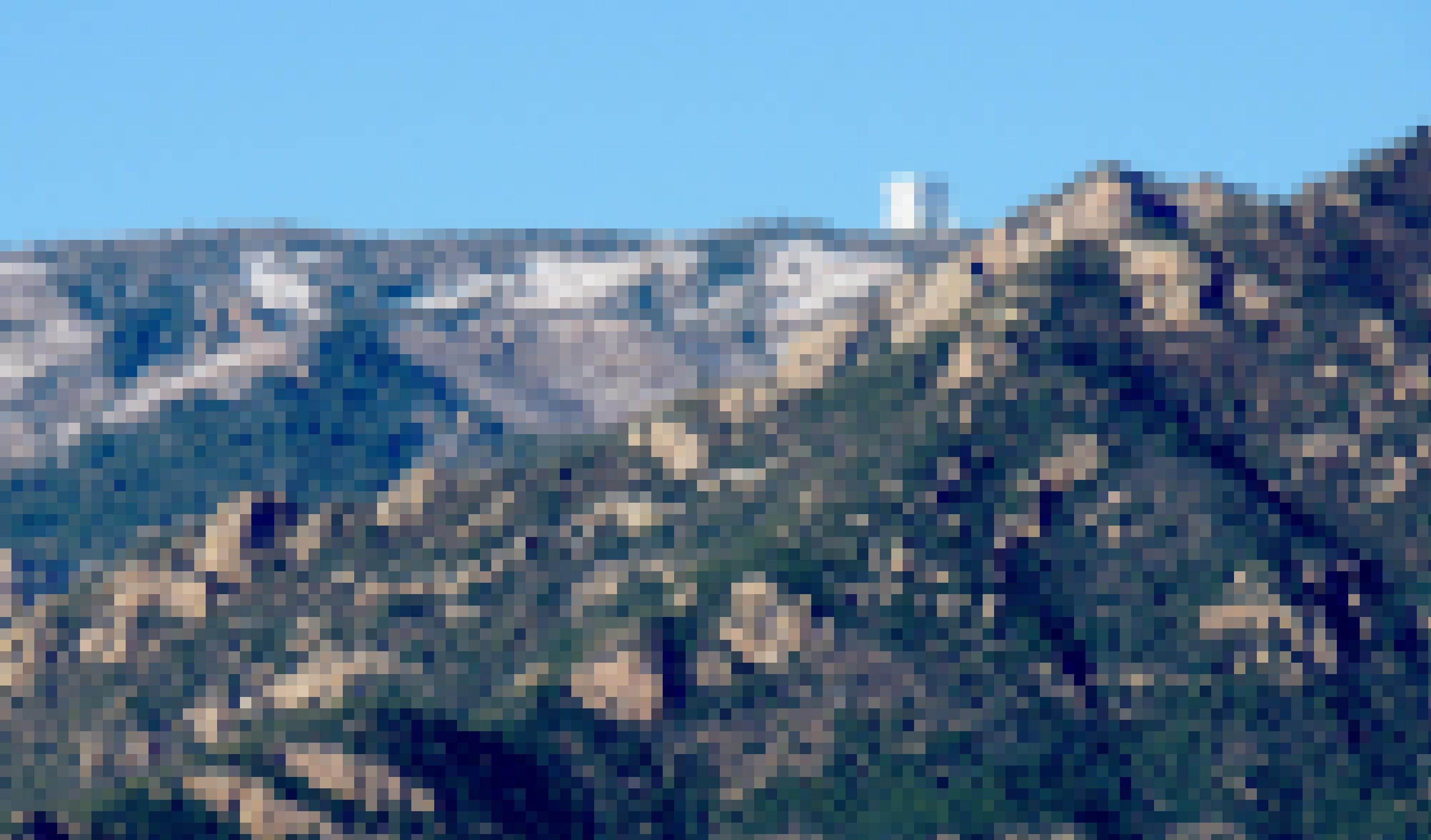 Ein teilweise begrünter Berggipfel, auf dem ein kastenförmiges Teleskopgebäude erkennbar ist.